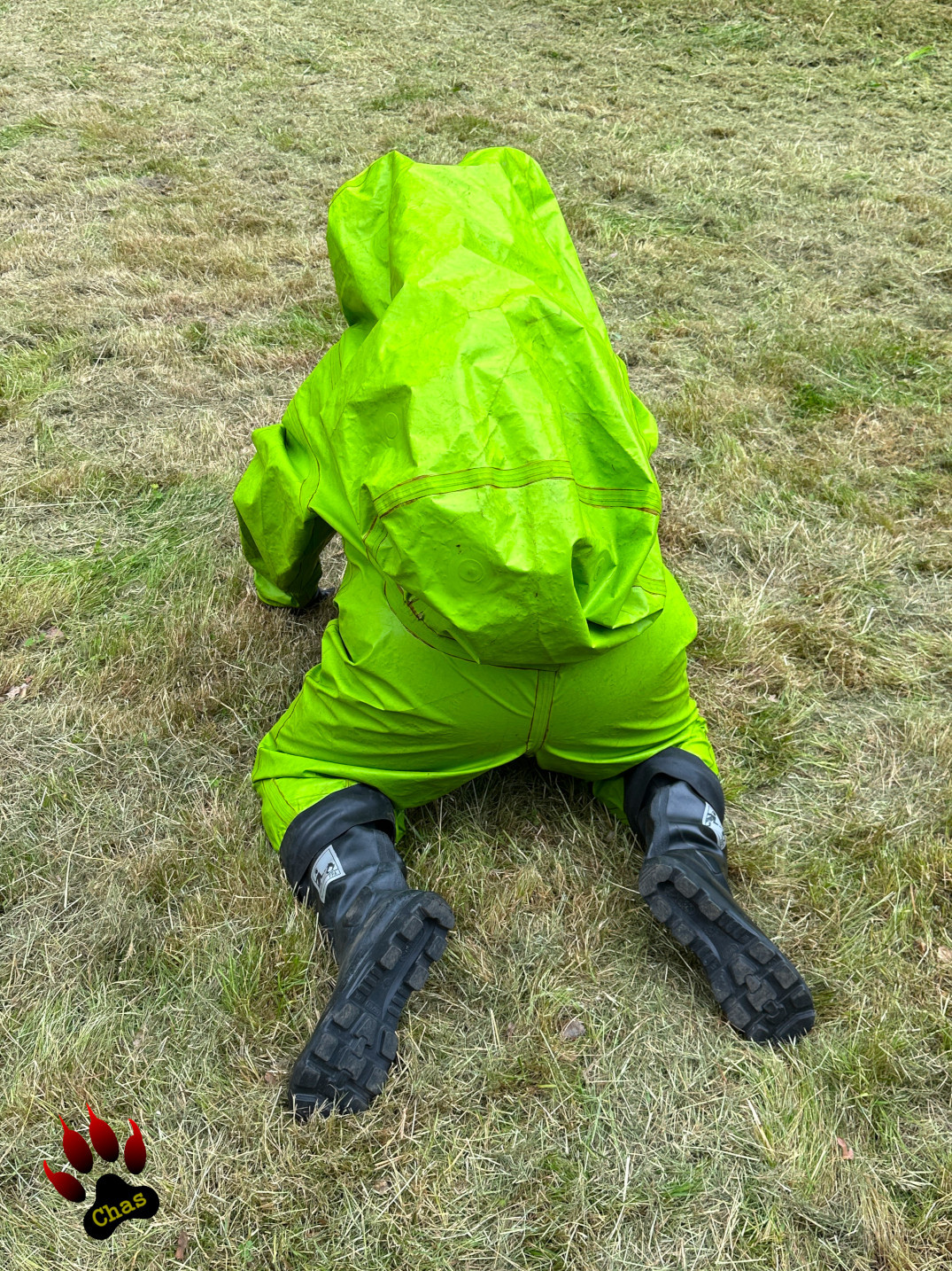 person in green hazmat suit with SCBA equipment sitting on a swing crawling over a freshly mowed lawn on all fours