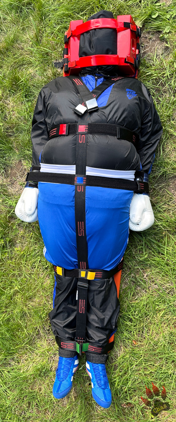 person in sweatsuit and boxing gear, wearing a headbag, tied to a spineboard, full view taken from above