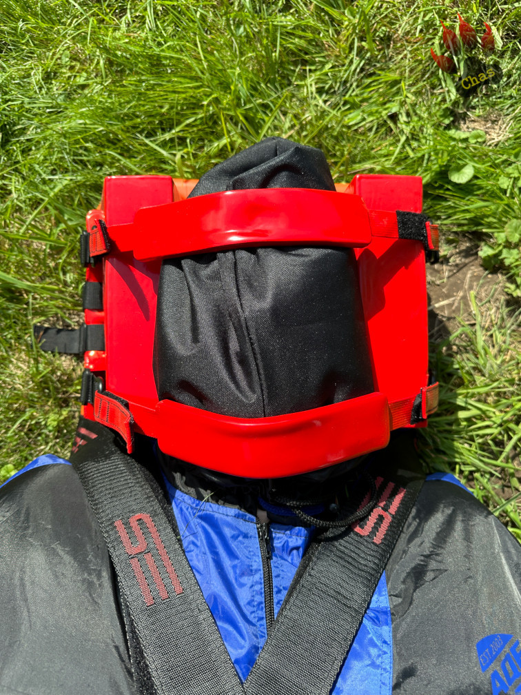 person in sweatsuit, wearing a headbag, tied to a spineboard, close up on head, taken from above