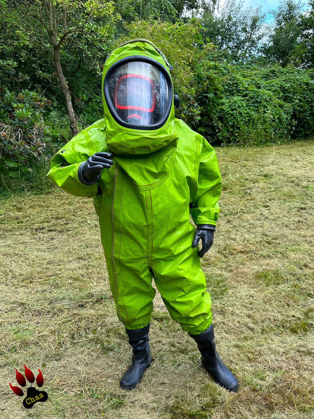 person in green hazmat suit with SCBA equipment standing on a freshly mowed lawn