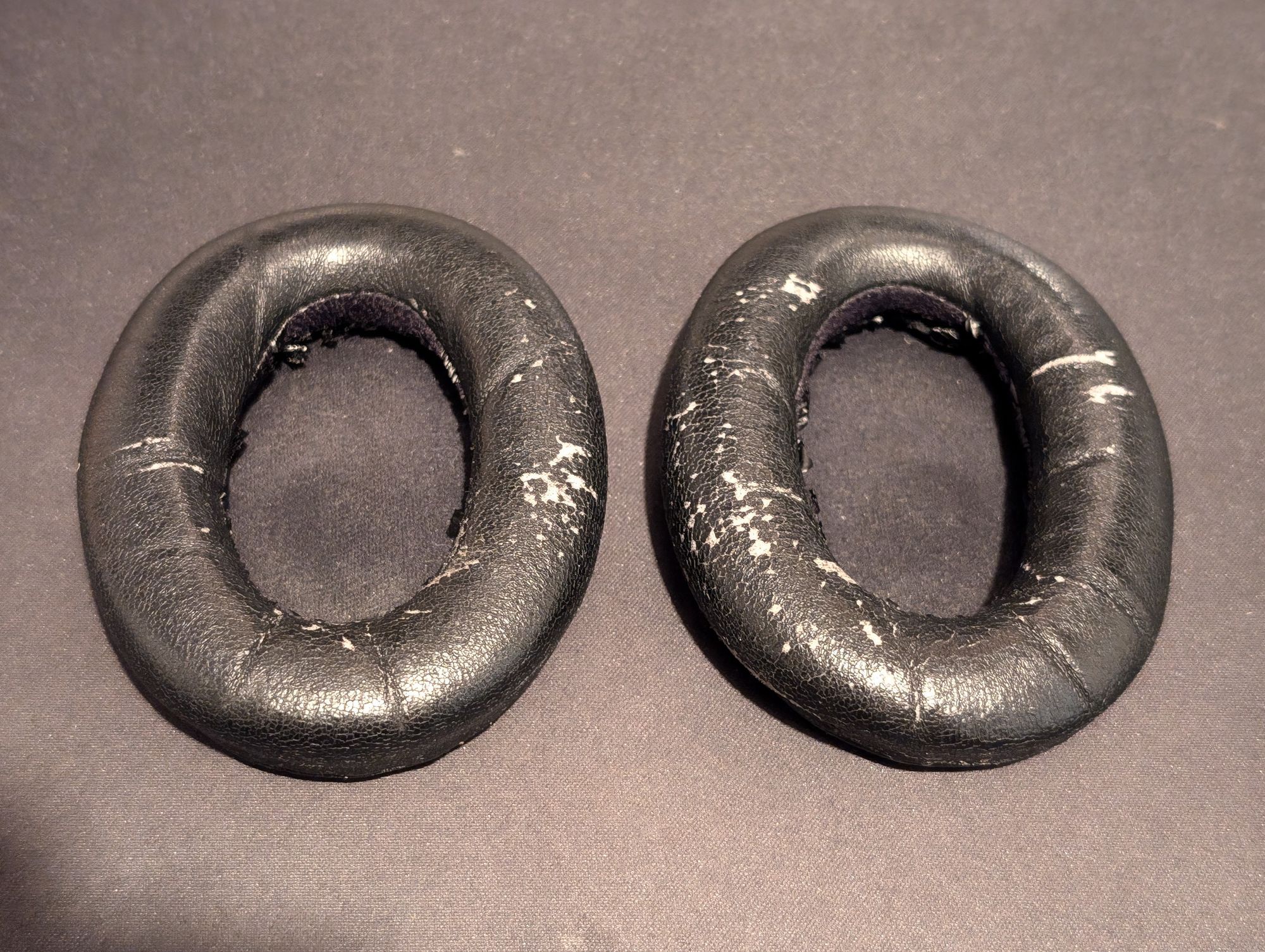 A pair of worn out headphone cushions. The leather-like material is flaking and they look a little misshapen.