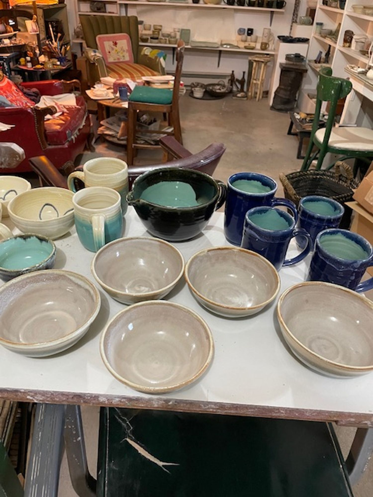 An array of wheel-thrown ceramic bowls and mugs, glazed turquoise, blue, ivory, and gray.