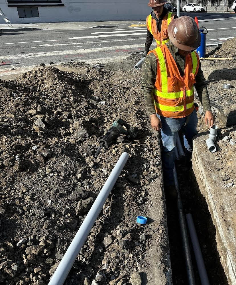 Crews in hard hats and reflective vests working on excavating for traffic signal conduits and pole foundations at 10th and Bryant streets.