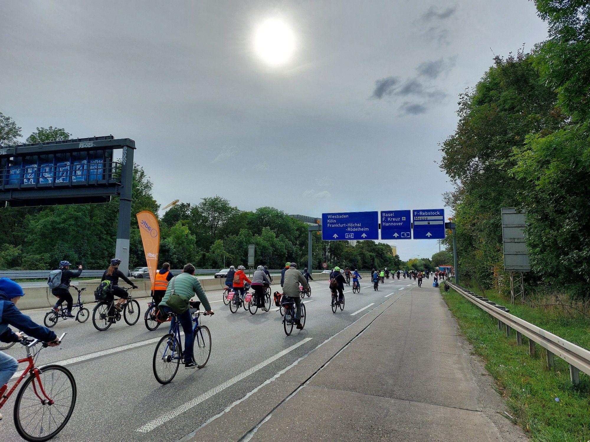 Viele Fahrradfahrer fahren auf der A648, im Hintergrund sieht man blaue Autobahn-Hinweisschilder.