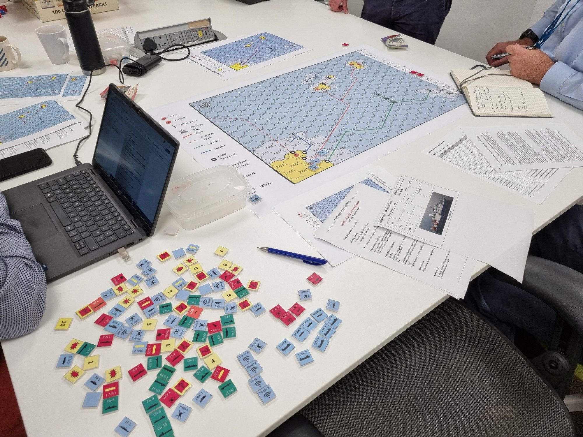 A table with a game map, pile of counters and a laptop, ready for a game of COBALT ROCKS.