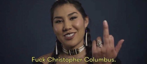 A picture of an indigenous woman holding up her middle finger. The picture is captioned Fuck Christopher Columbus.