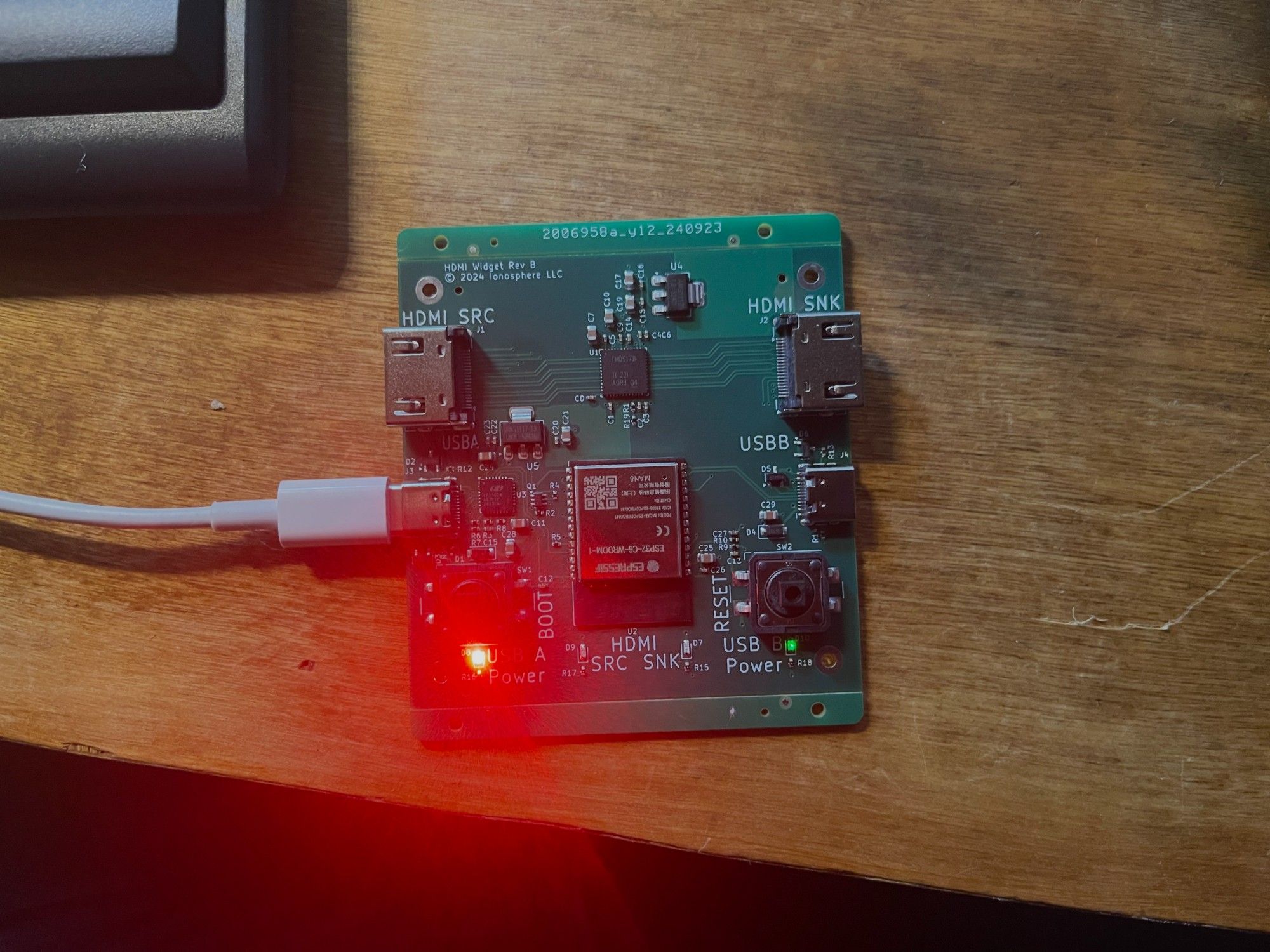 The same circuit board as before, but with a USB-C cable plugged in on the left (USB-A) port. A red LED in the bottom left corner is shining brightly and overloading my phone's camera, spraying errant rays elsewhere.