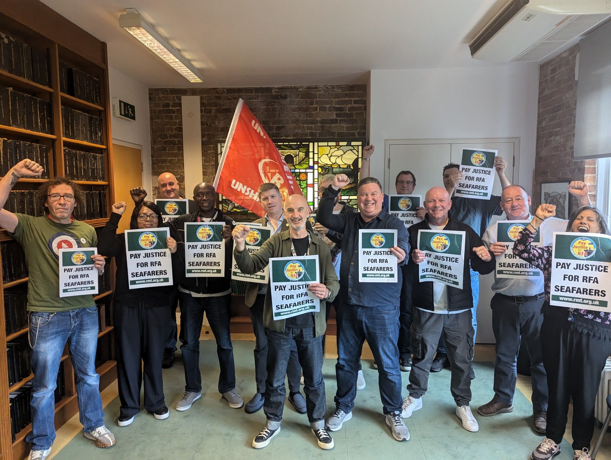 RMT NEC members standing in the RMT boardroom hold placards demanding Pay Justice For RFA seafarers to mark World Maritime Day