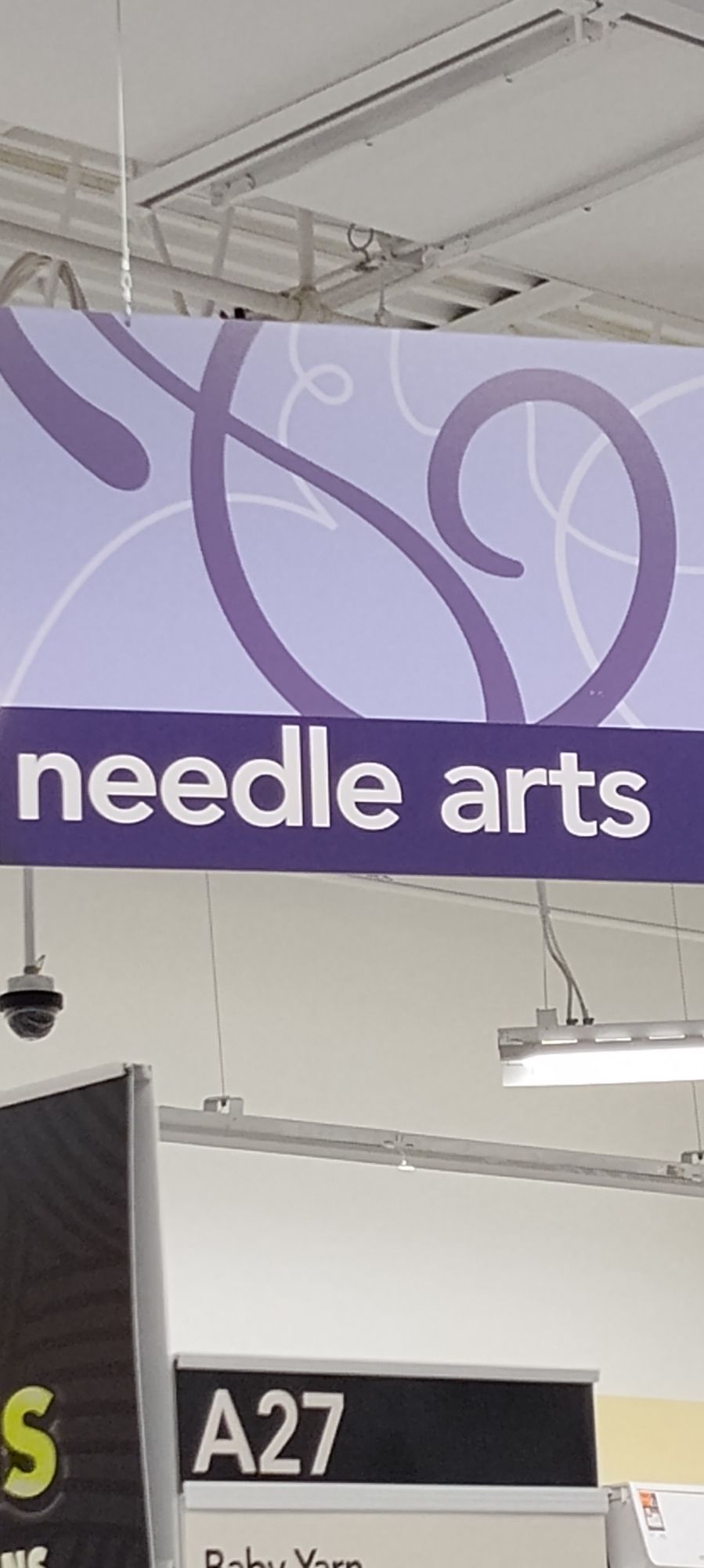 A picture of a sign in joann's denoting the supplies sold in that section. It says "needle arts"