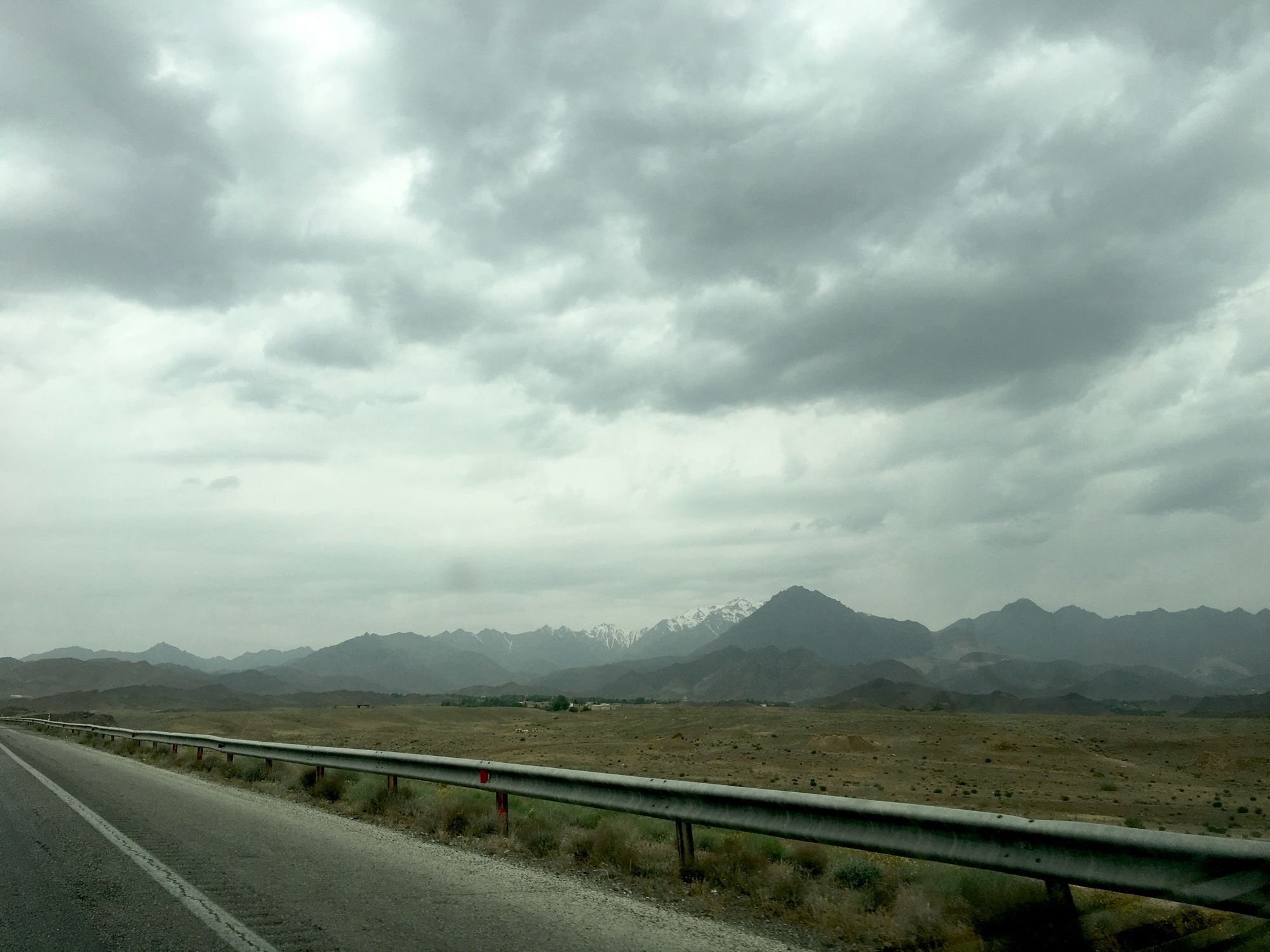 Grey skies, almost bare flat landscape; in the distance mountains (probable also quite bare), some snow covered