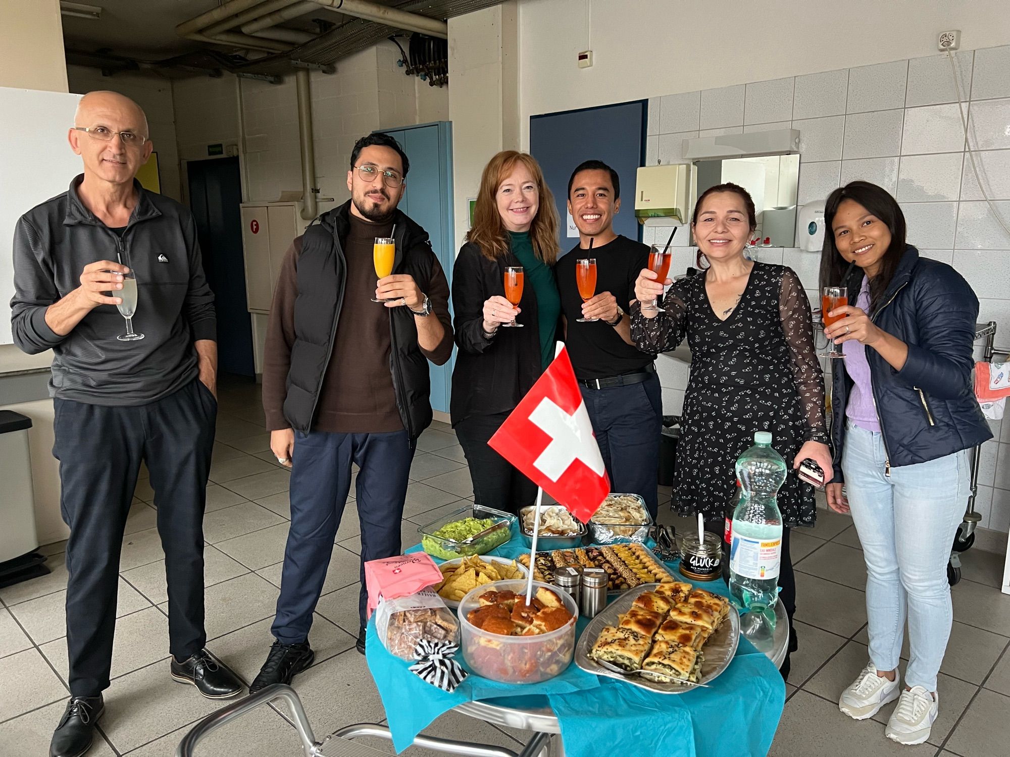 3 Männer und 3 Frauen stehen um gedecktes Tischchen mit Essen und Schweizer Flagge