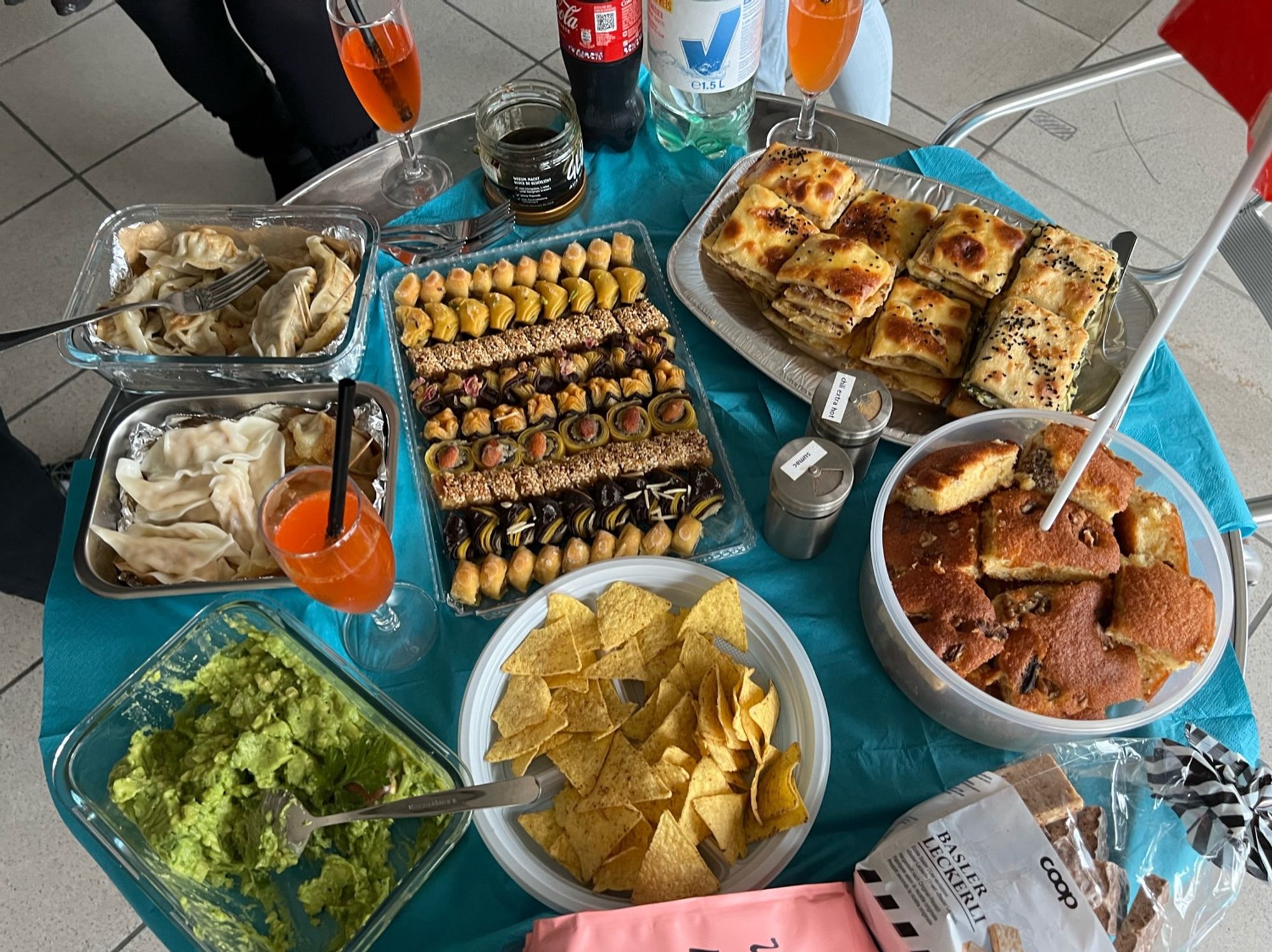 Tisch mit Gyoza, Guacamole & Chips, Basler Läckerli, Nusskuchen, Börek, afghanische Süssigkeiten. Cola, Aperol.