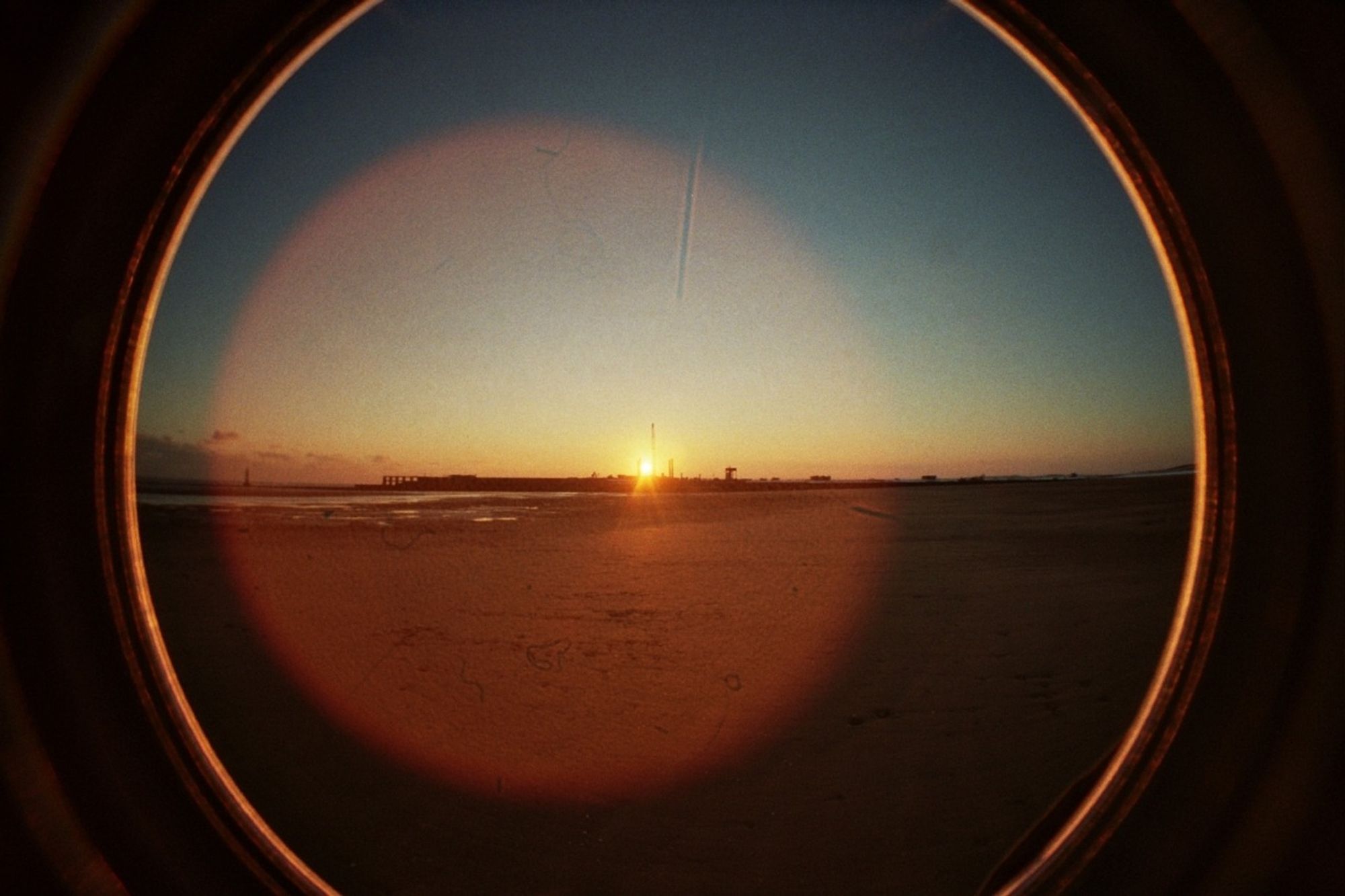 A fisheye photo of a beach at sunset with lots of lens flare