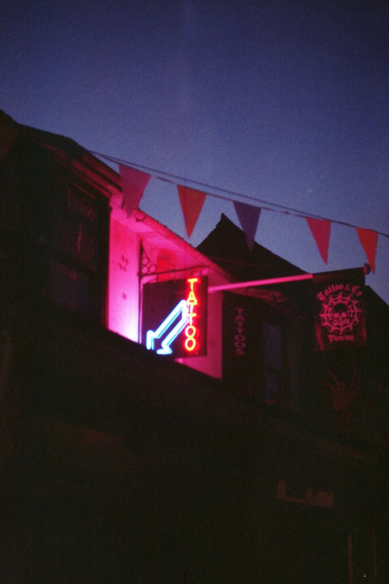 A night photo of a building with a bright neon "tattoo" sign