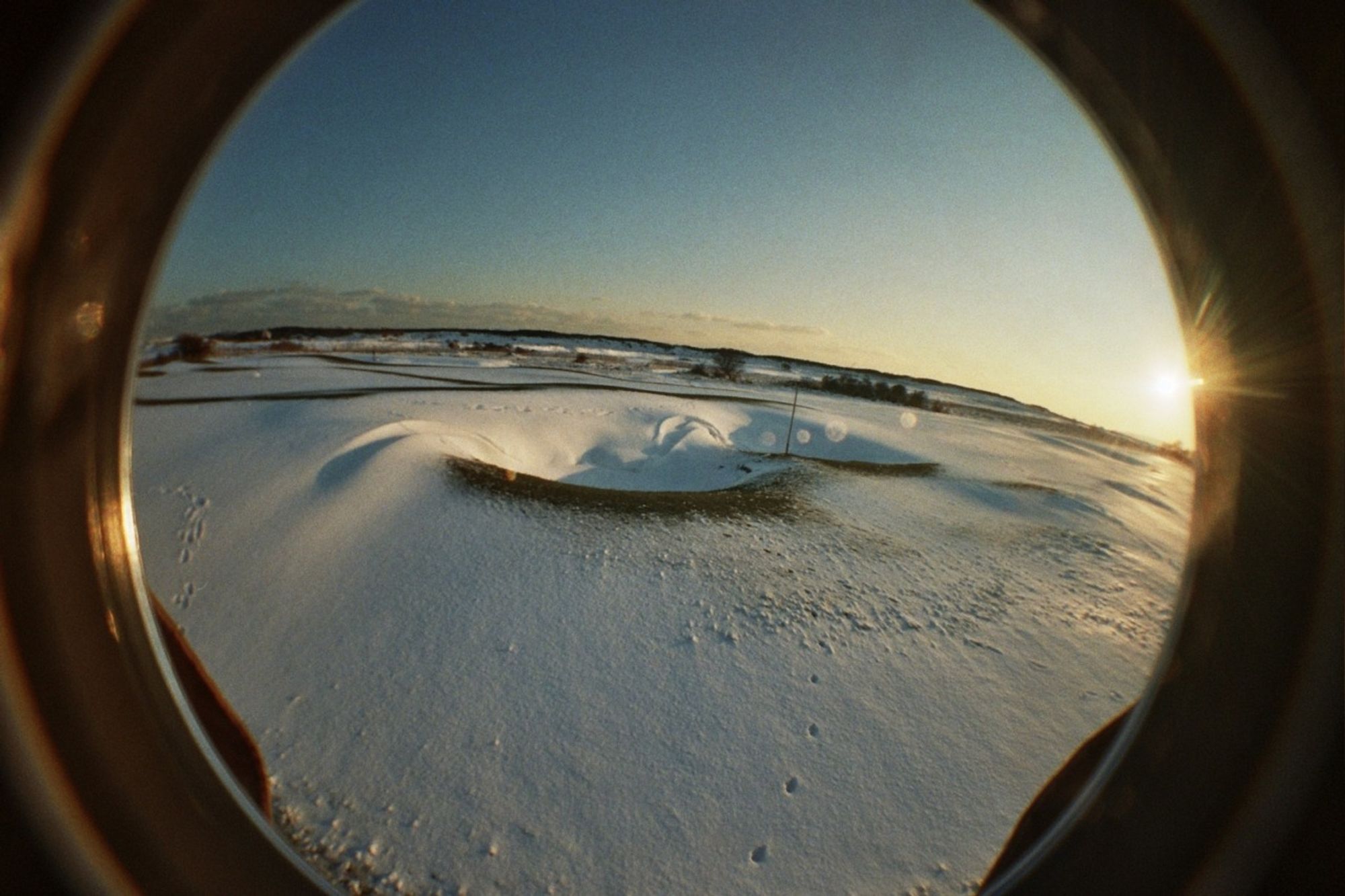 A fisheye view of a beach at sunset, covered in snow, with long shadows