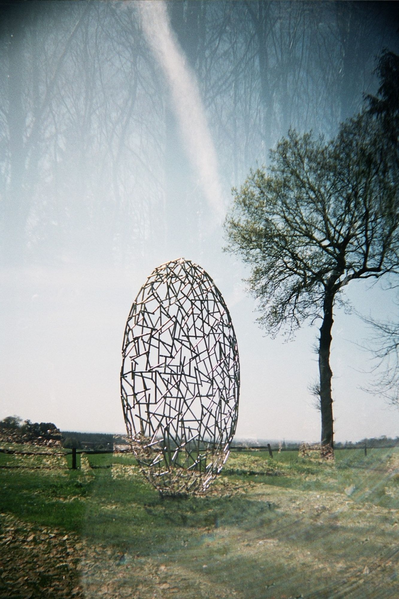 a double exposure of a round, doughnut like sculpture make of short metal rods in the sunglight