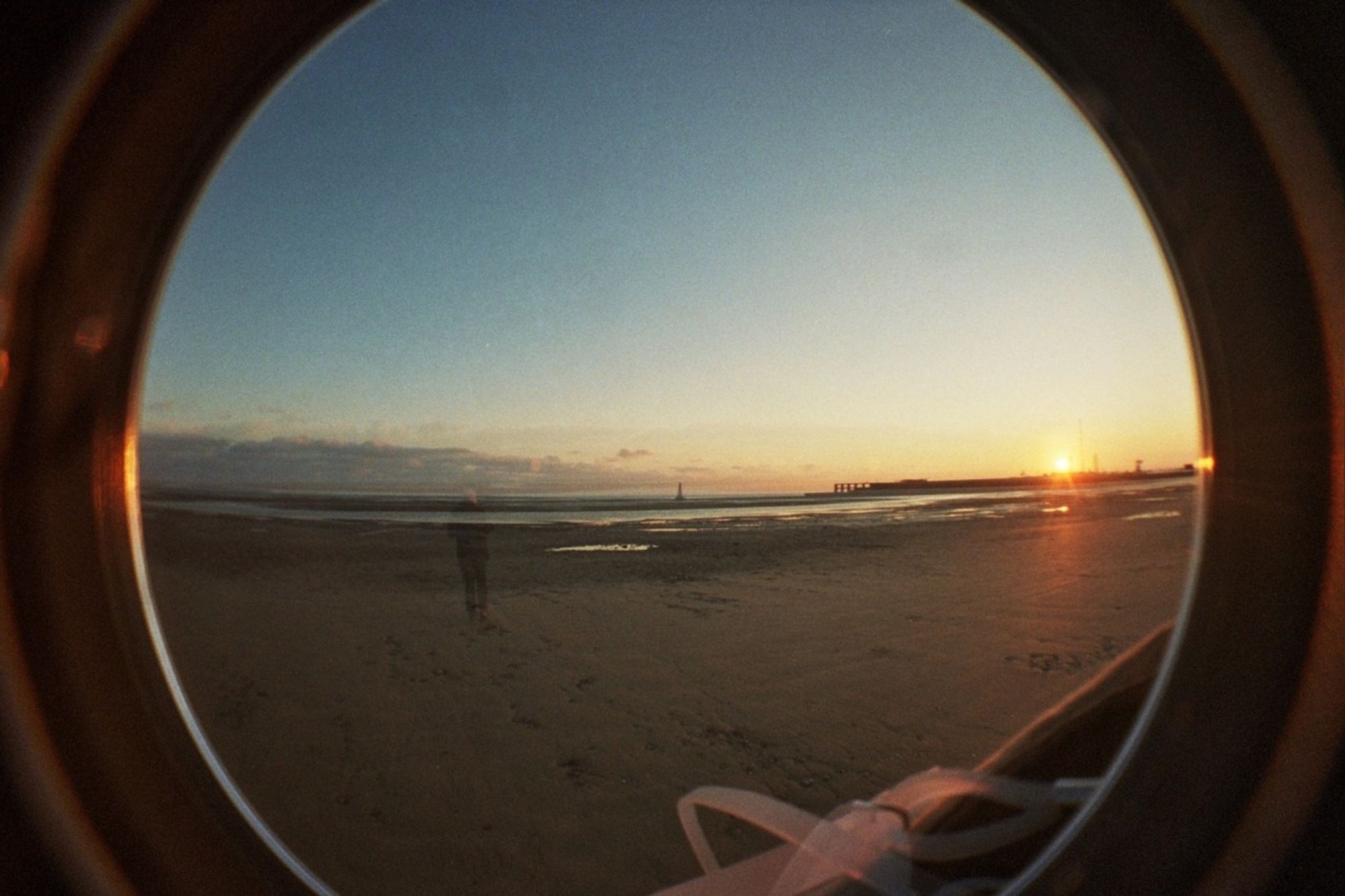 a double exposure fisheye photo of a beach at sunset. a ghostly figure is just visible to the left