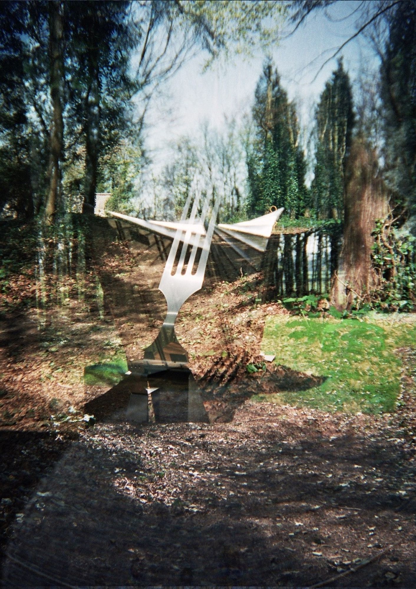 A double exposure photo of a sculpture in the woods in the sunlight of a giant fork