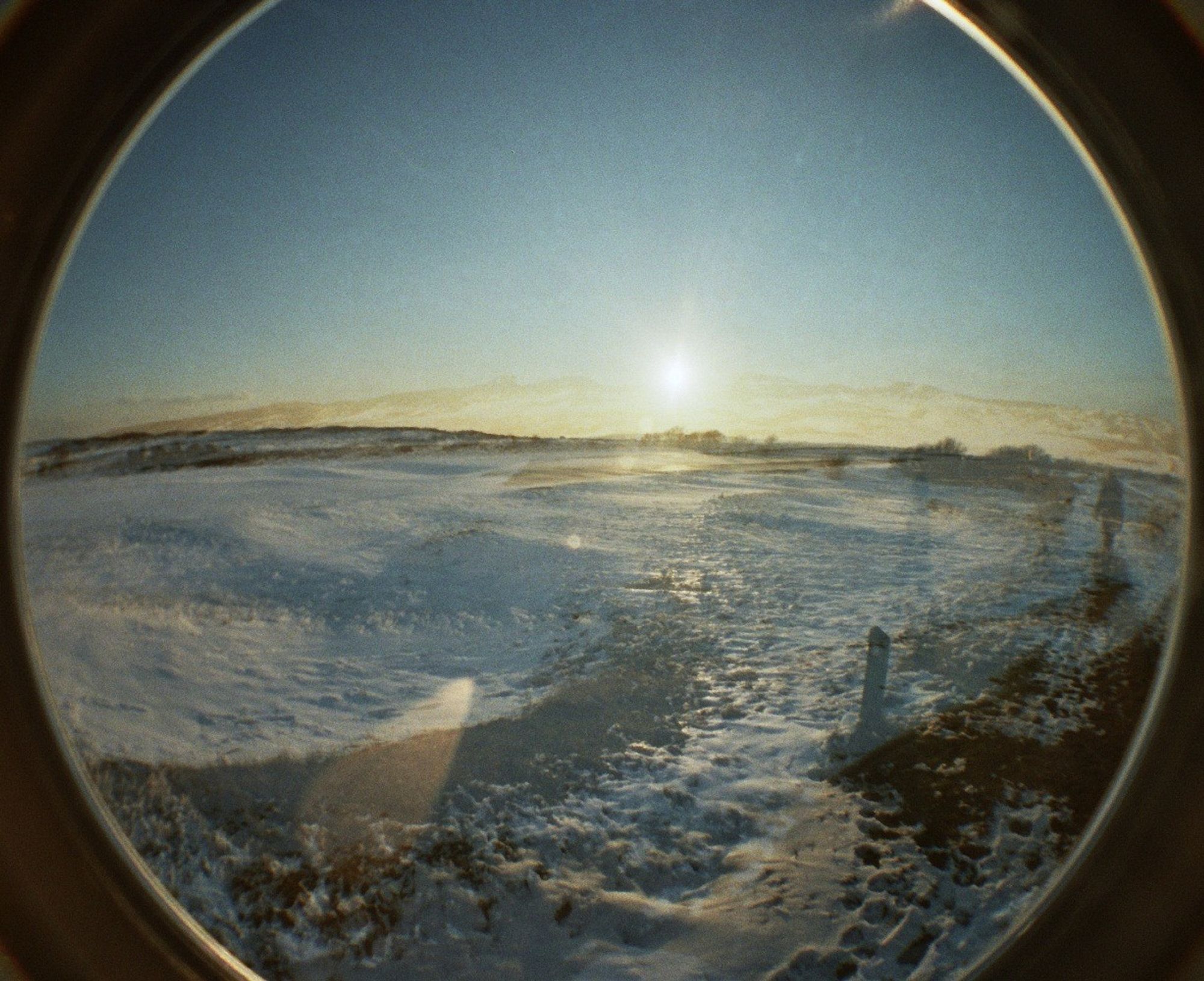 a double exposure fisheye photo of a snow covered beach at sunset. a ghostly figure is just visible to the right