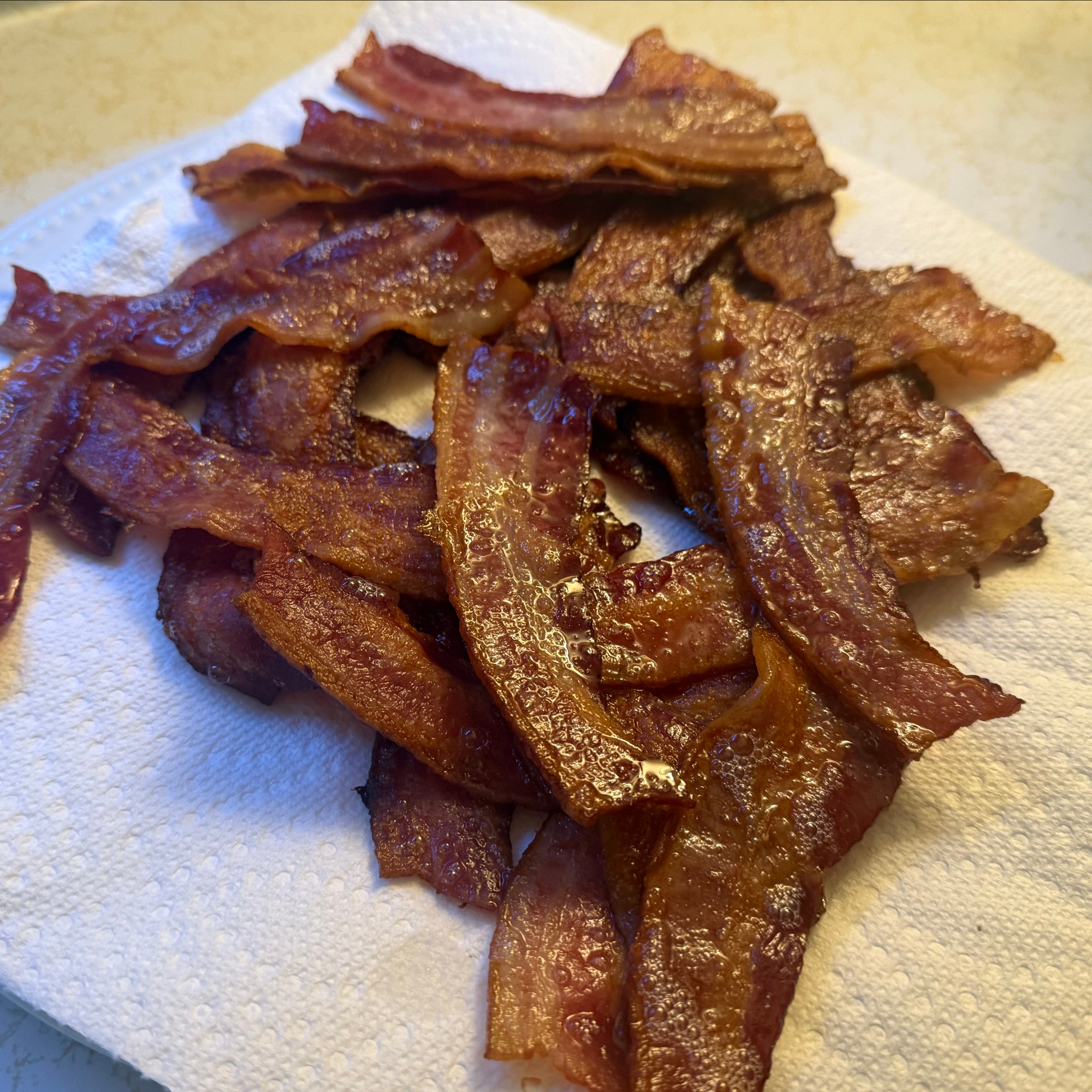 Small pile of baked golden brown bacon glistening with grease plated with paper towel