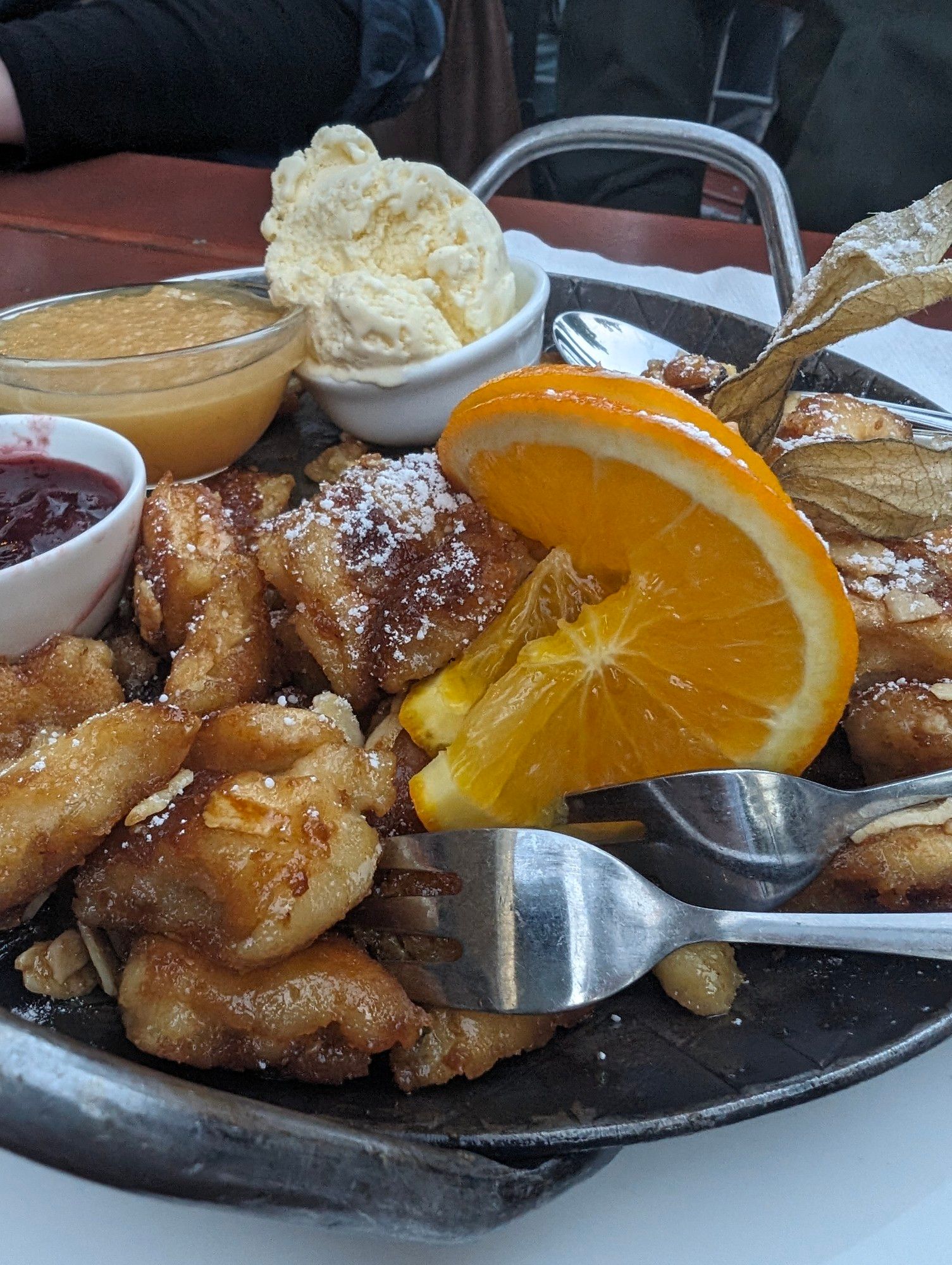 Ein Teller Kaiserschmarrn mit Orangenscheiben als Deko, dazu Schälchen mit Zwetschgenröster, Apfelmus und Vanilleeis.