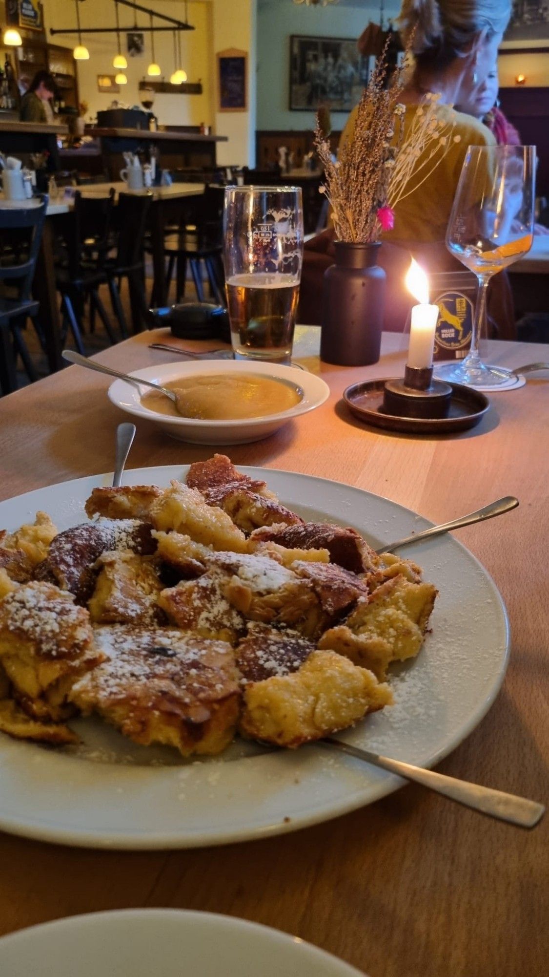 Ein Teller mit Kaiserschmarrn, im Hintergrund ein Teller mit Apfelmus, 1 Glas Bier und eine Kerze. Eine sehr romantische Stimmung.