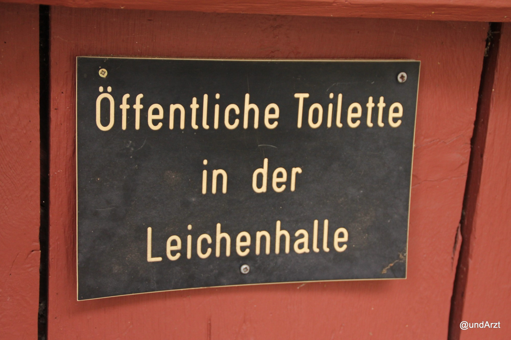 Schild auf Holztür: "Öffentliche Toilette in der Leichenhalle"