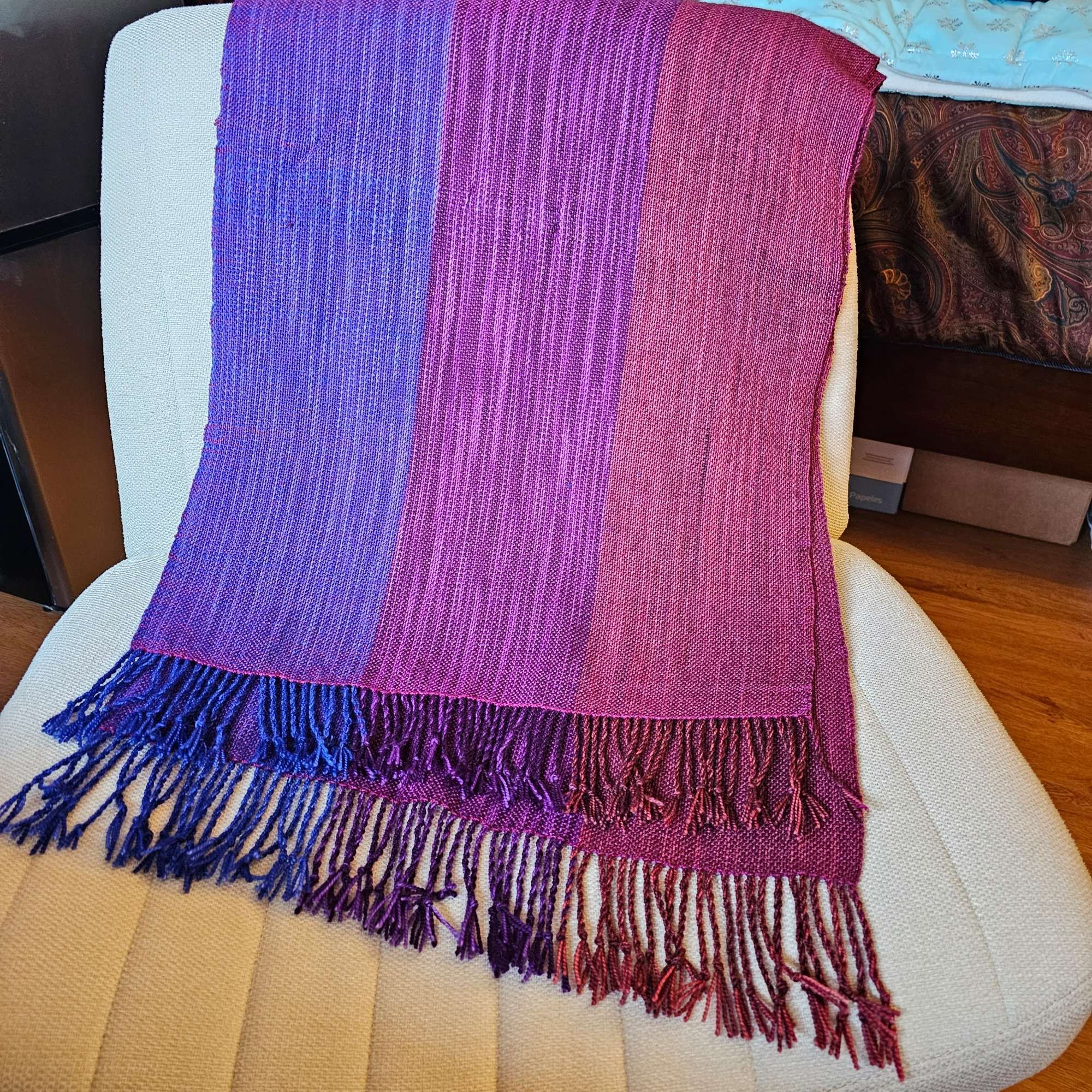 A woven shawl in blue, purple, and red, with a twisted fringe edge.