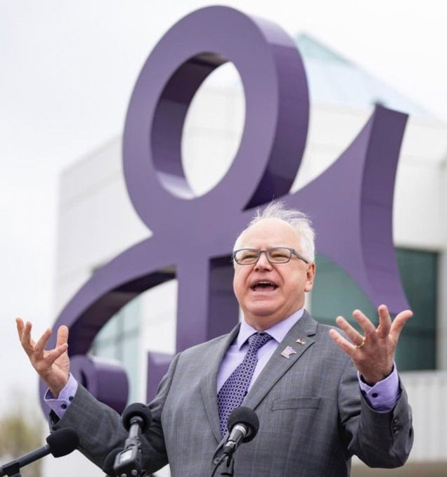 Tim Walz wearing purple in front of a giant Prince symbol