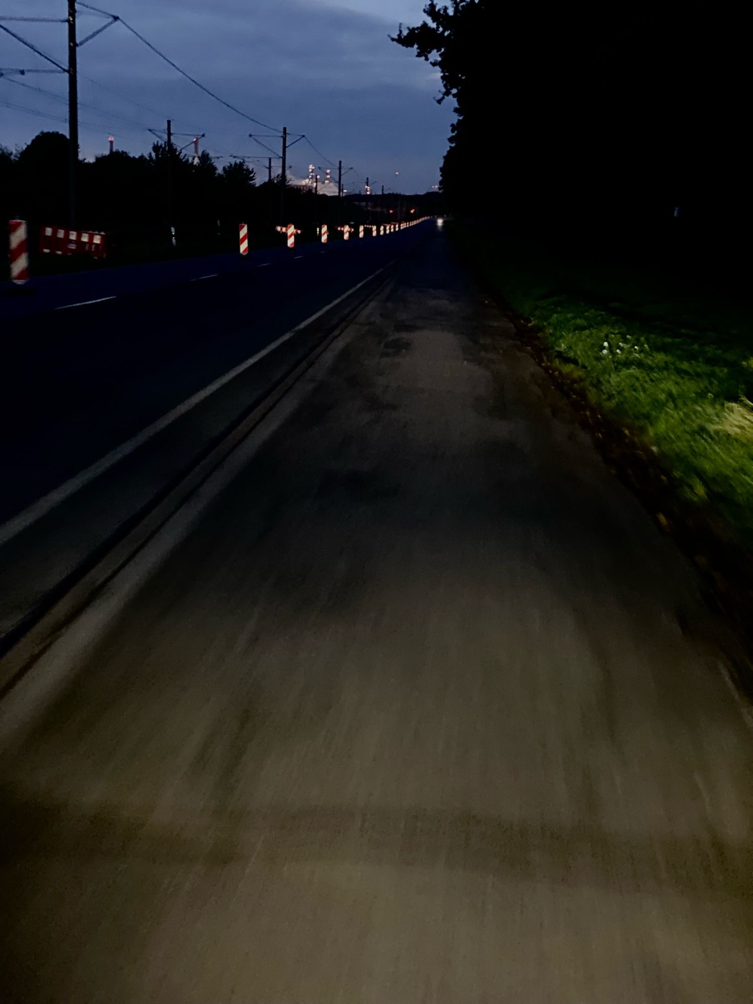 Die leere Industriestrasse im Dunkeln. Baken beleuchtet durch ein Fahrradlicht. Perspektive des Erstellers auf dem Fahrrad.