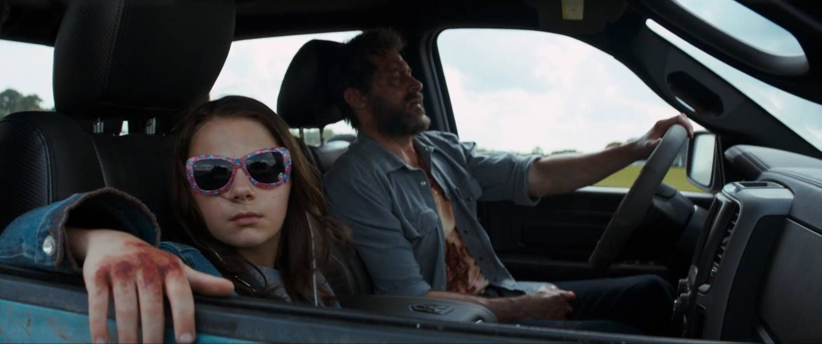 Screenshot from the movie LOGAN, a man is driving a car with a little girl next to him