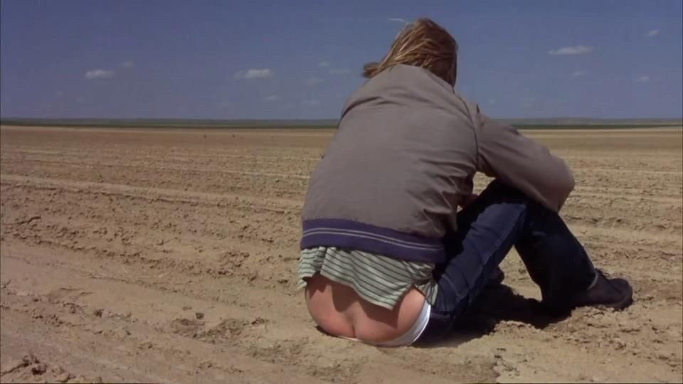 A shot taken from Dumb and Dumber. Jeff Daniels is sitting on the ground, alone, in an empty area.