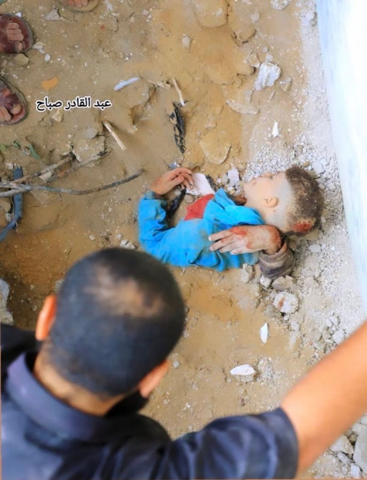 Half a torso of a boy in collapsed building with an arm of his brother still stick underneath hugging him in death