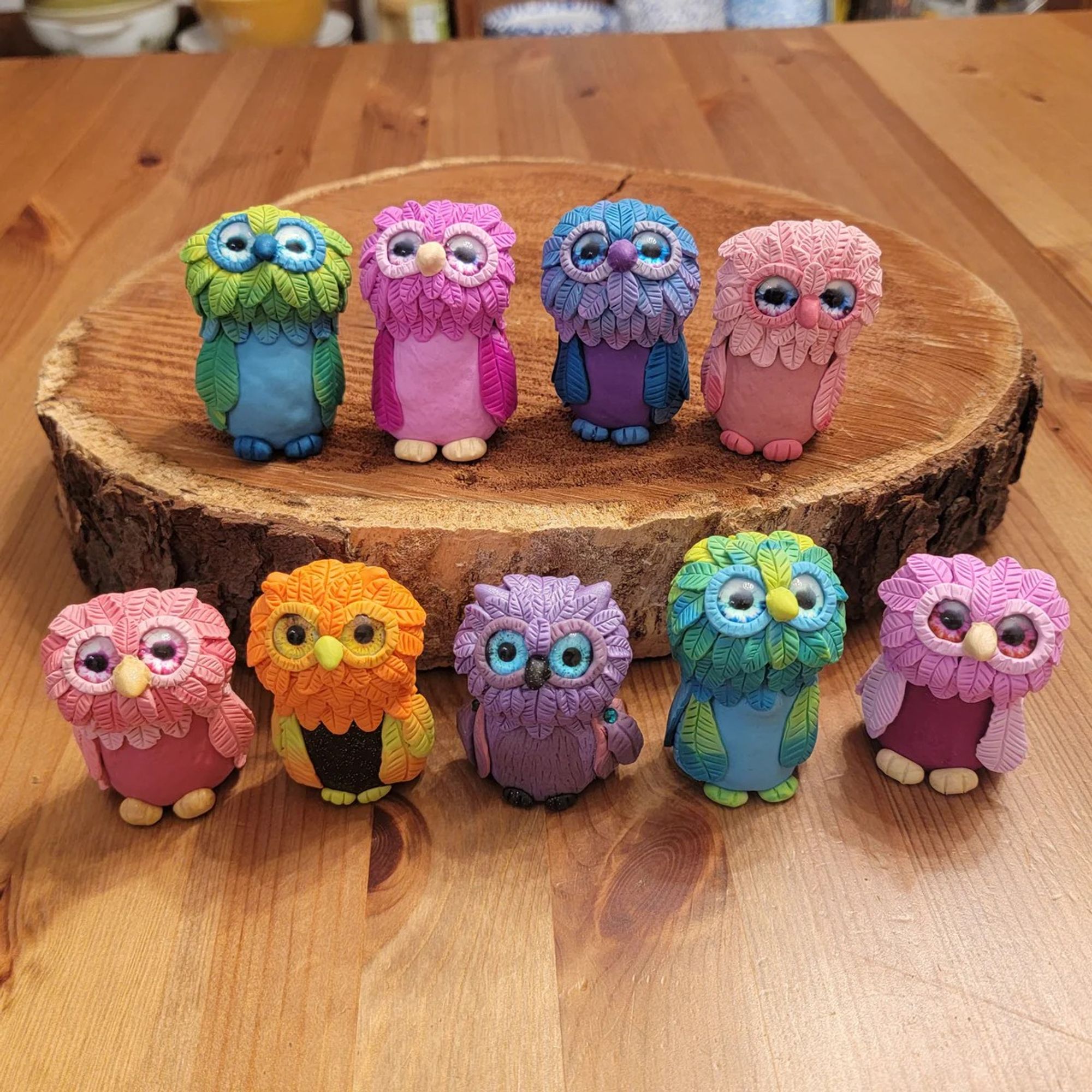 Two rows of colorful polymer clay owls lined up on a table and a piece of wood.