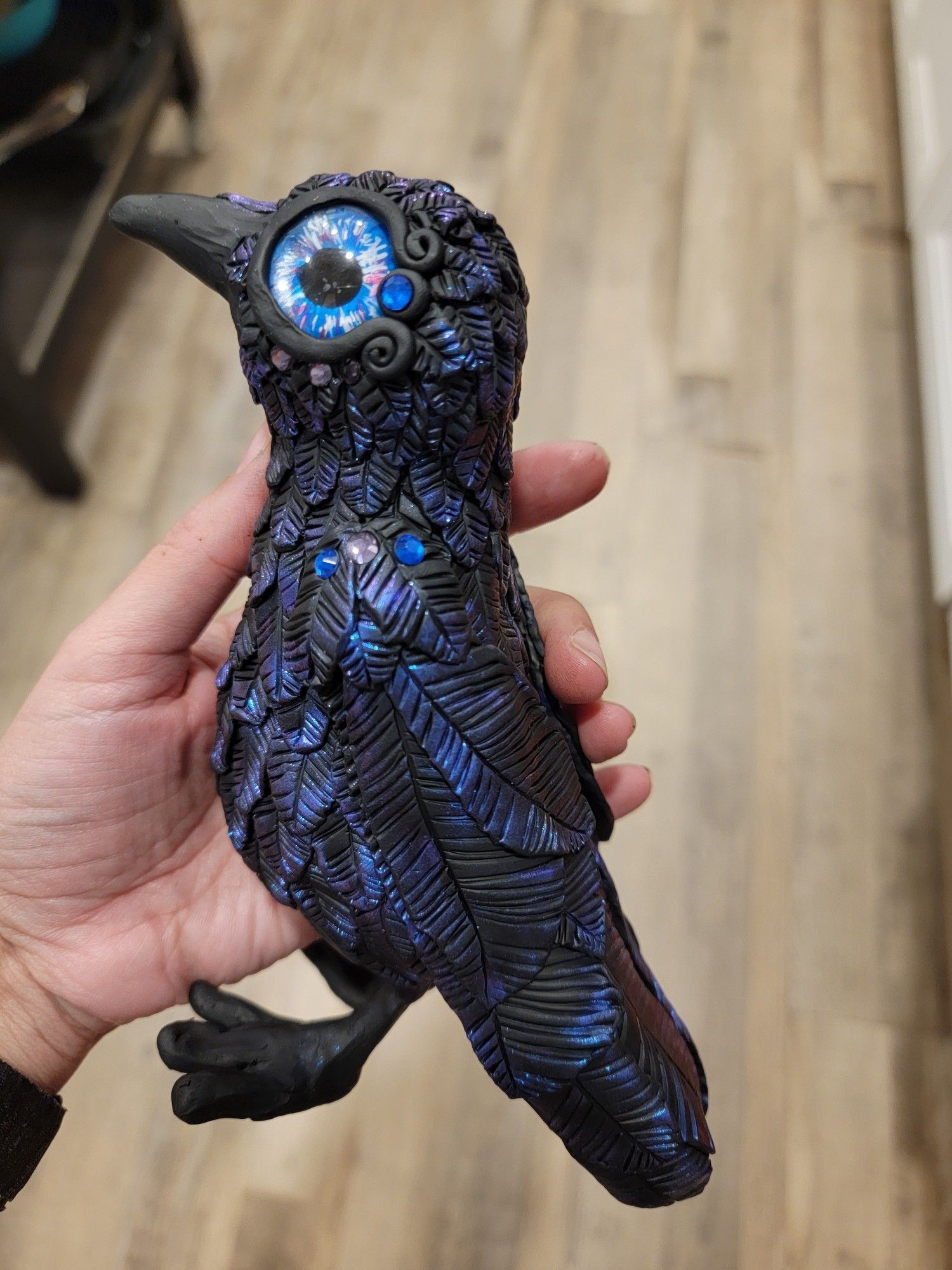 A hand holding a large polymer clay crow with shiny feathers