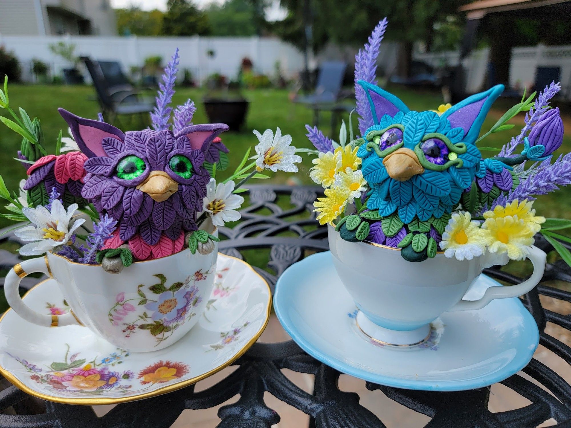 Two colorful griffins sitting in teacups surrounded by flowers.