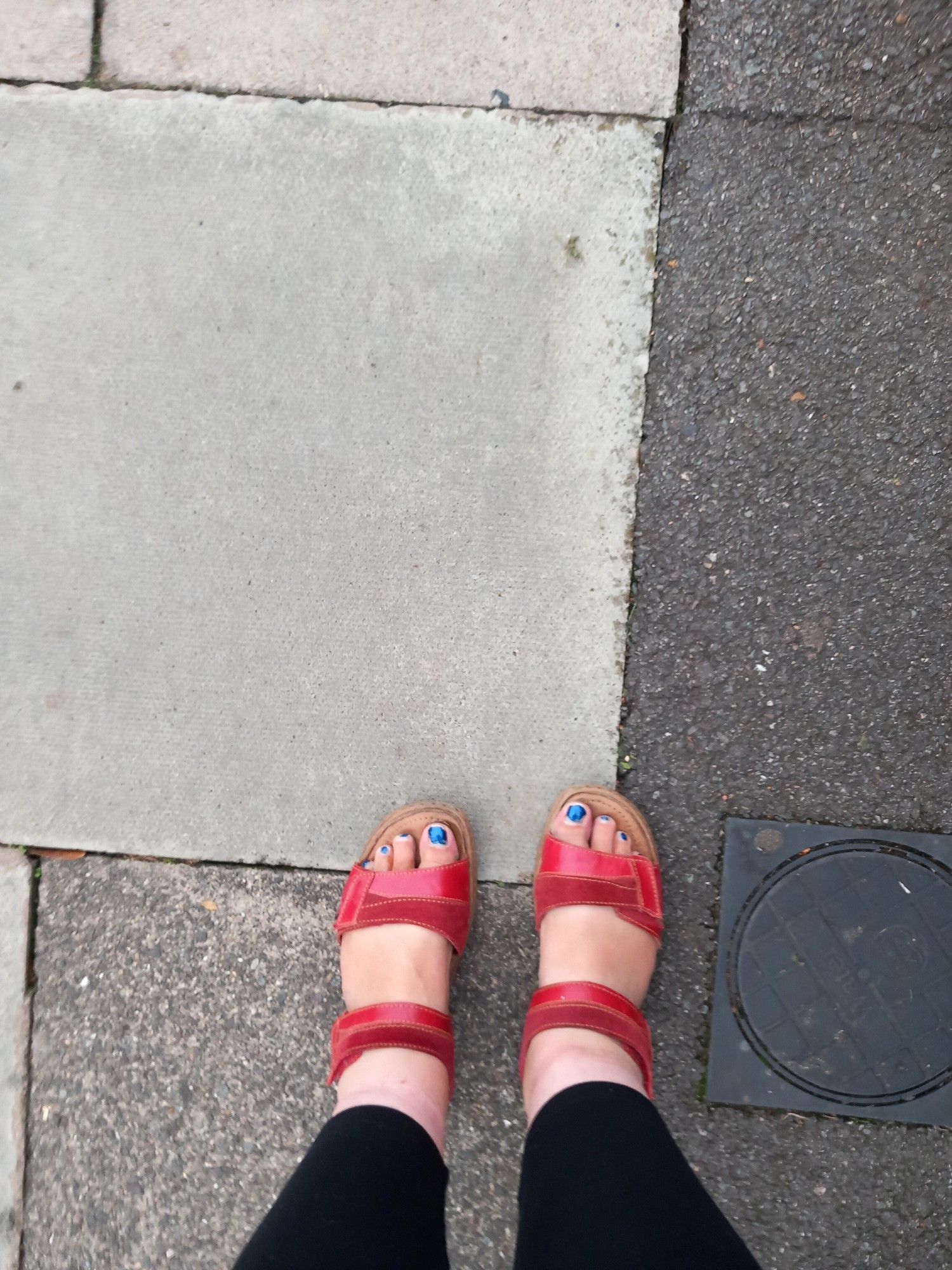 Feet in red sandals on damp pavement