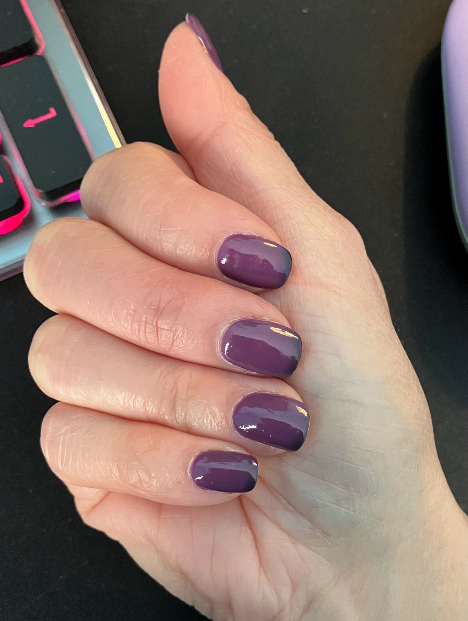 Closed hand showing nails painted in a deep grey/rose color with darker, almost plum to black nail tips.