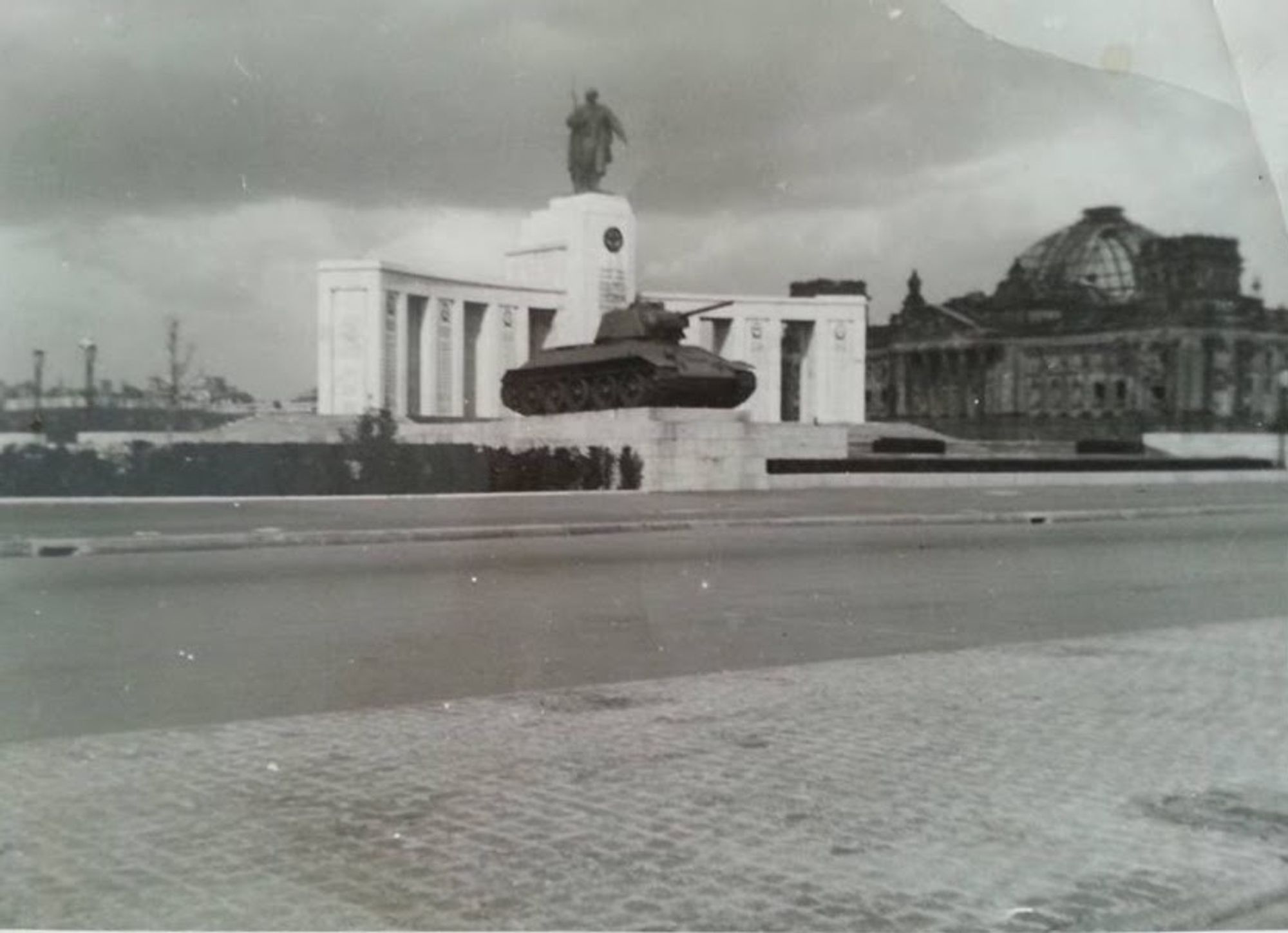 A black and white photograph of the soviet war memorial in Berlin. The ruins of the Reichstag in the background.