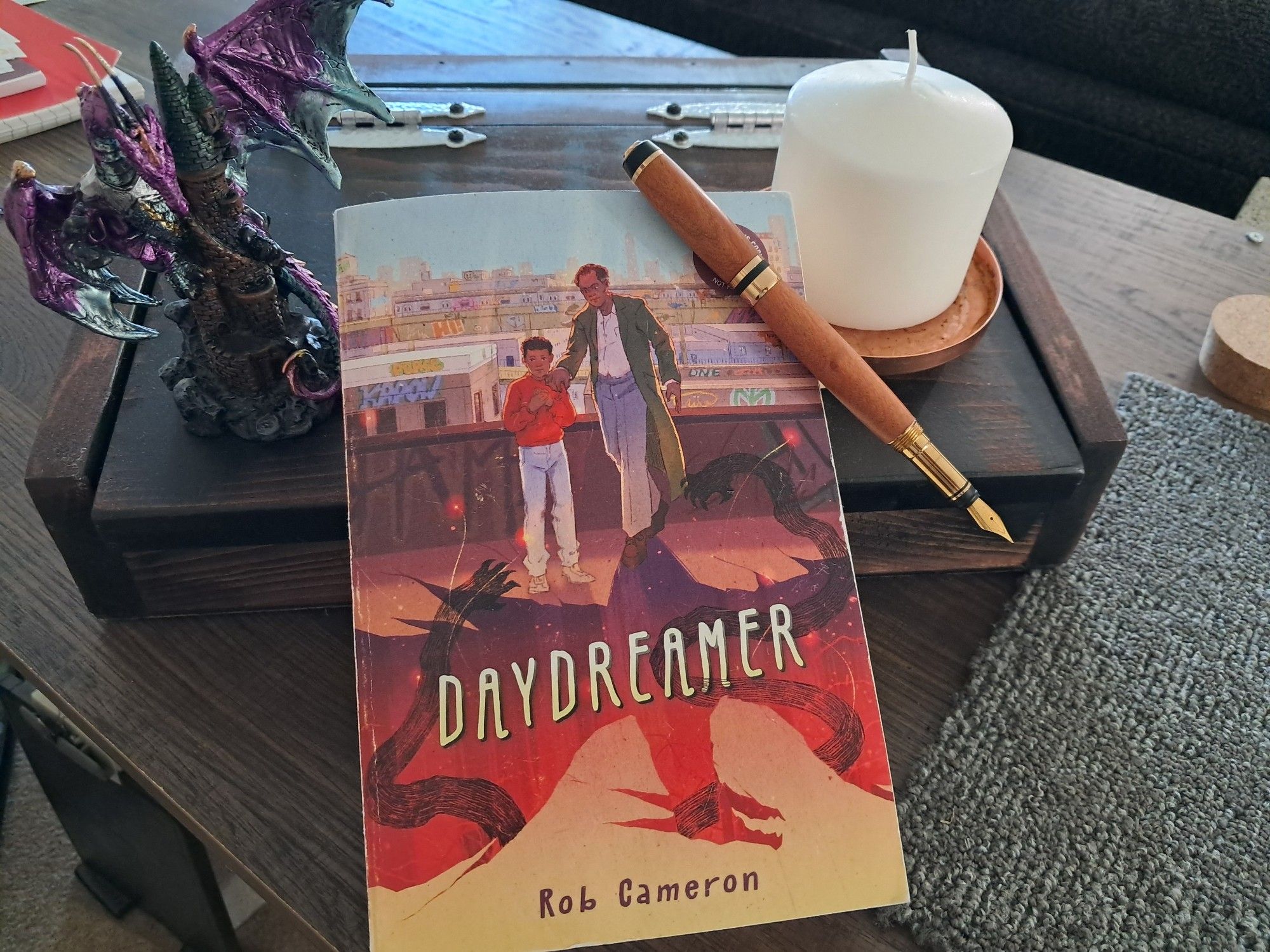 Cover of novel DAYDREAMER, featuring a young boy being consoled by an elderly man whose shadow is a dragon.