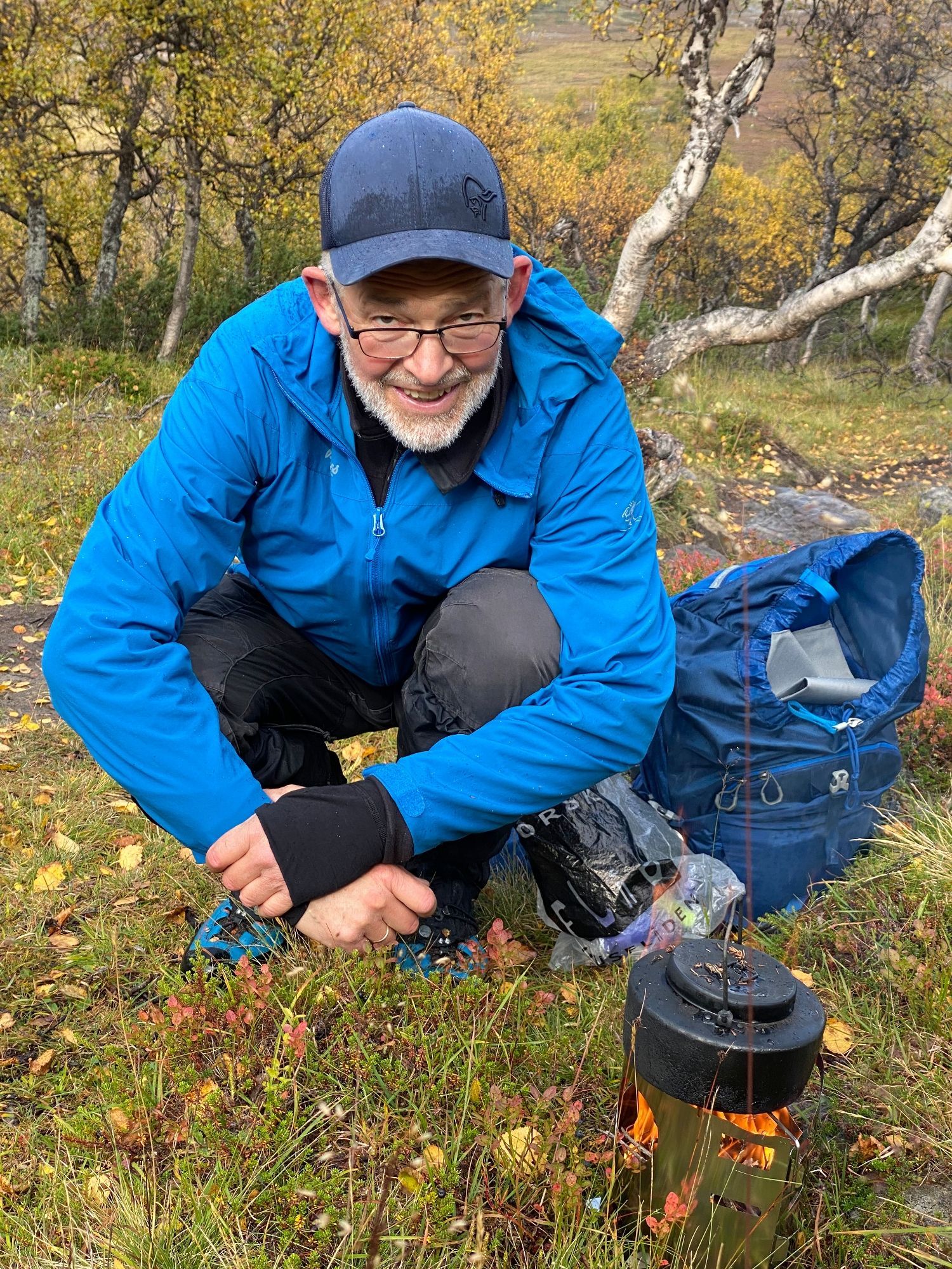 Jeg (mann i blå anorakk med ditto caps og sekk, på huk) koker kaffe i svartkjel på kvistbrenner