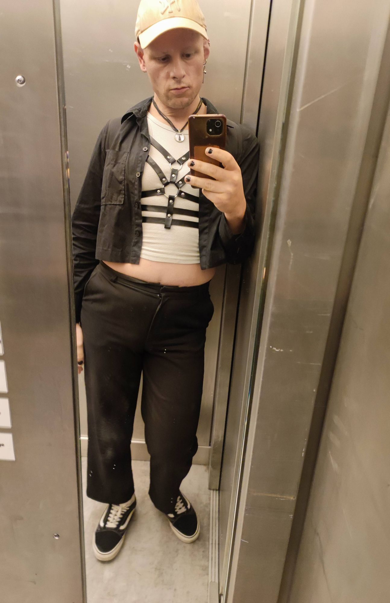 Selfie von mir im Aufzug. Ich trage schwarze Hose, weißes crop top, harness und schwarzes Hemd.