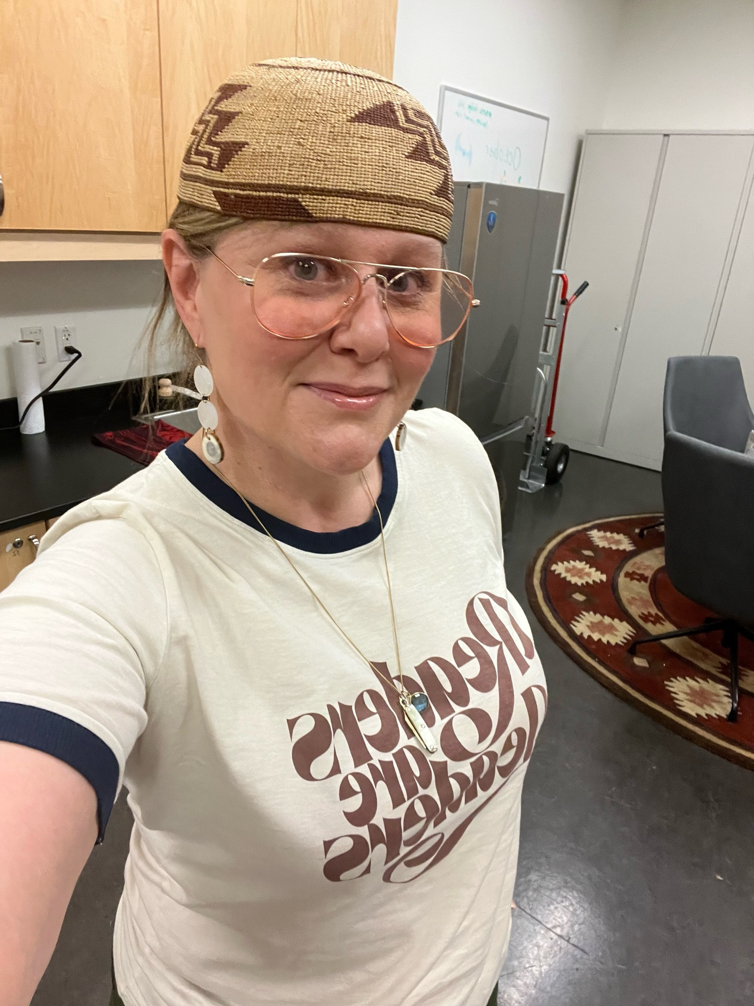 me standing there in selfie mode looking like I’m not terrified of public speaking. I’m wearing a Readers Are Leaders ringer tee, my pink aviator reading glasses and a basket cap. Woodshop teacher core.