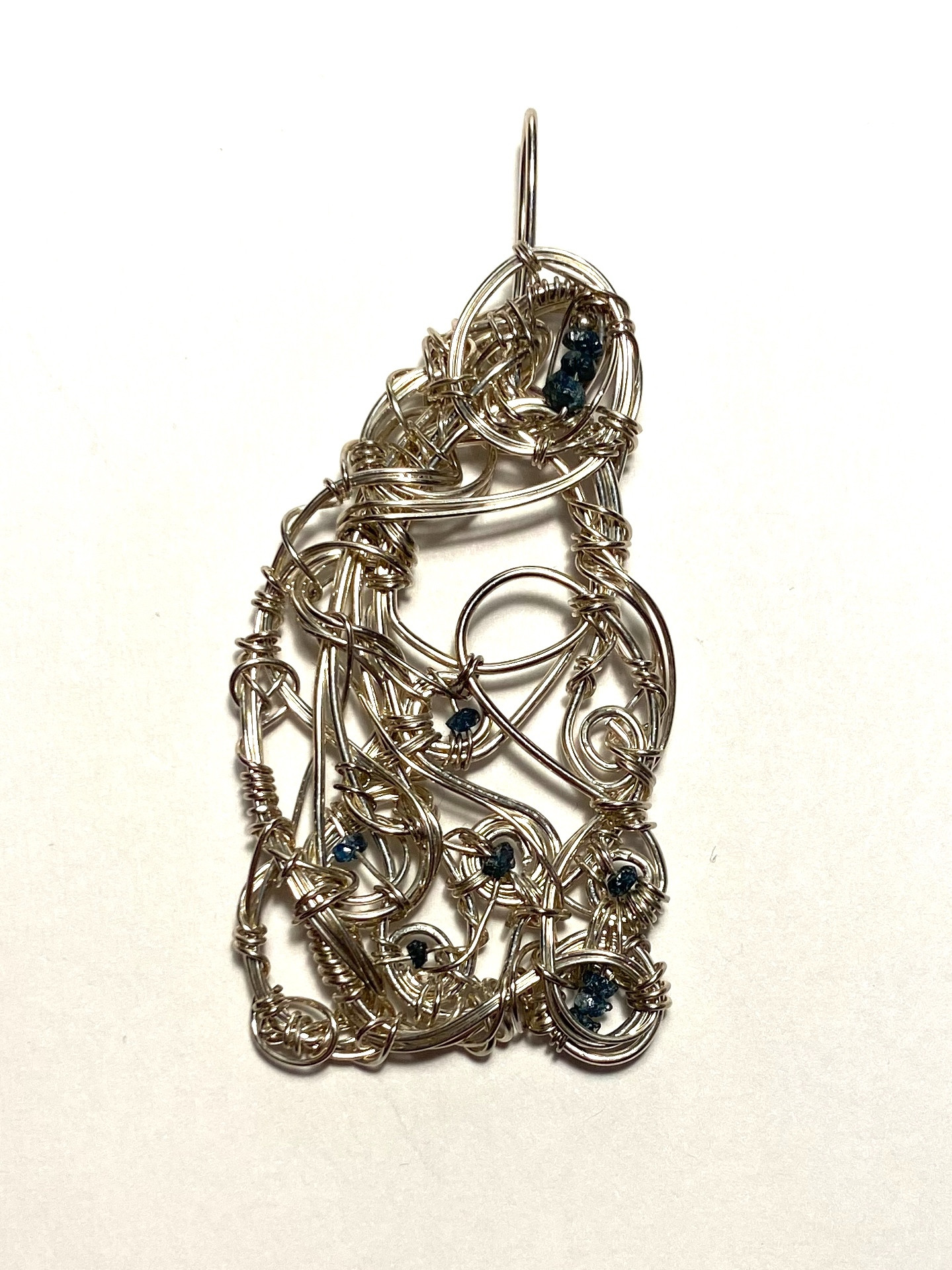 This freeform handmade sterling silver wirework pendant looks rather like a cloaked figure in profile, heading somewhere to take care of something. If you look closely, there are eleven small drilled rough pieces of a blue stone. Those are natural blue diamonds. (References and supplier available on request.)