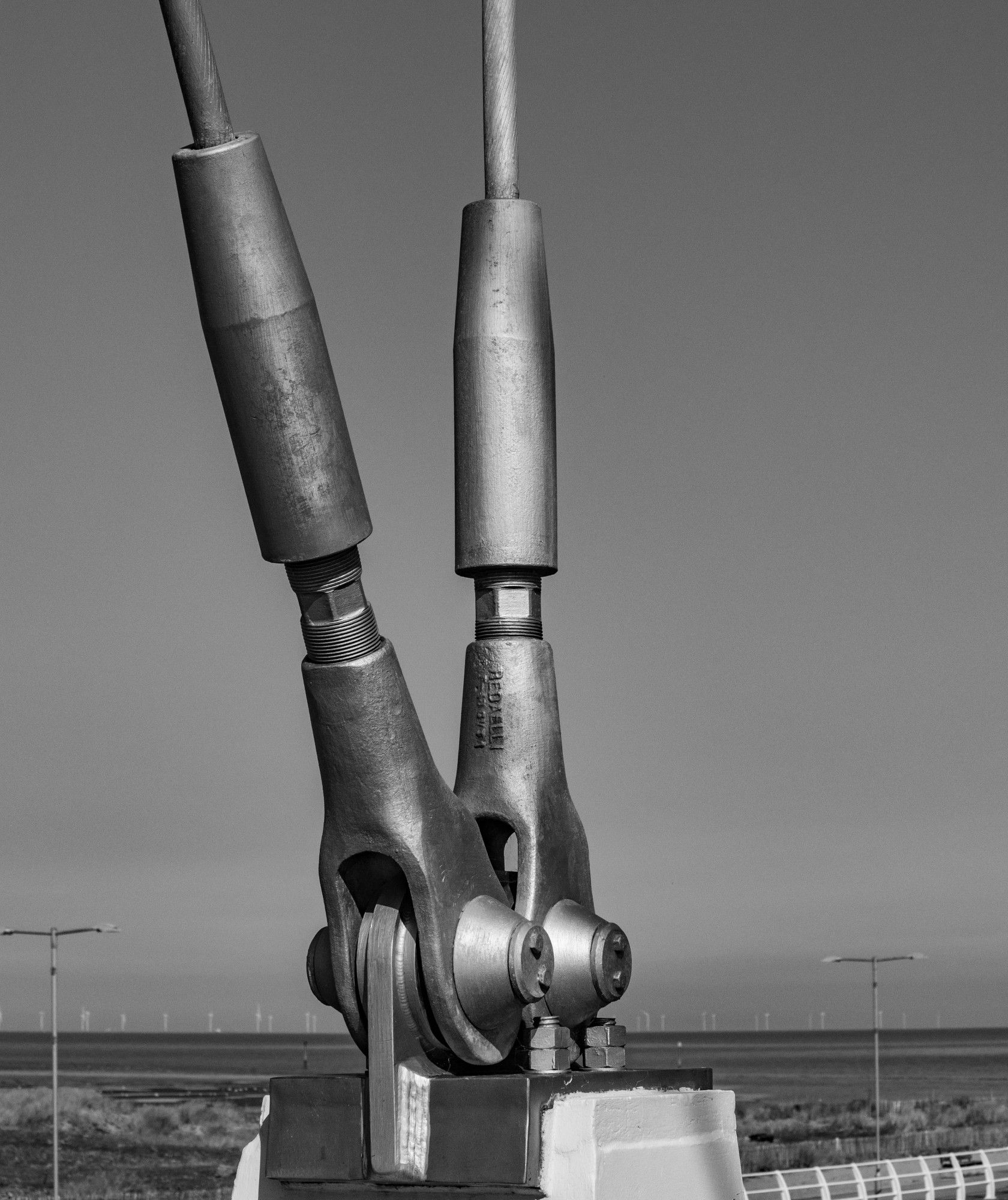 A close-up monochrome image showing two metal supports attached to a bridge, suspending the walkway.