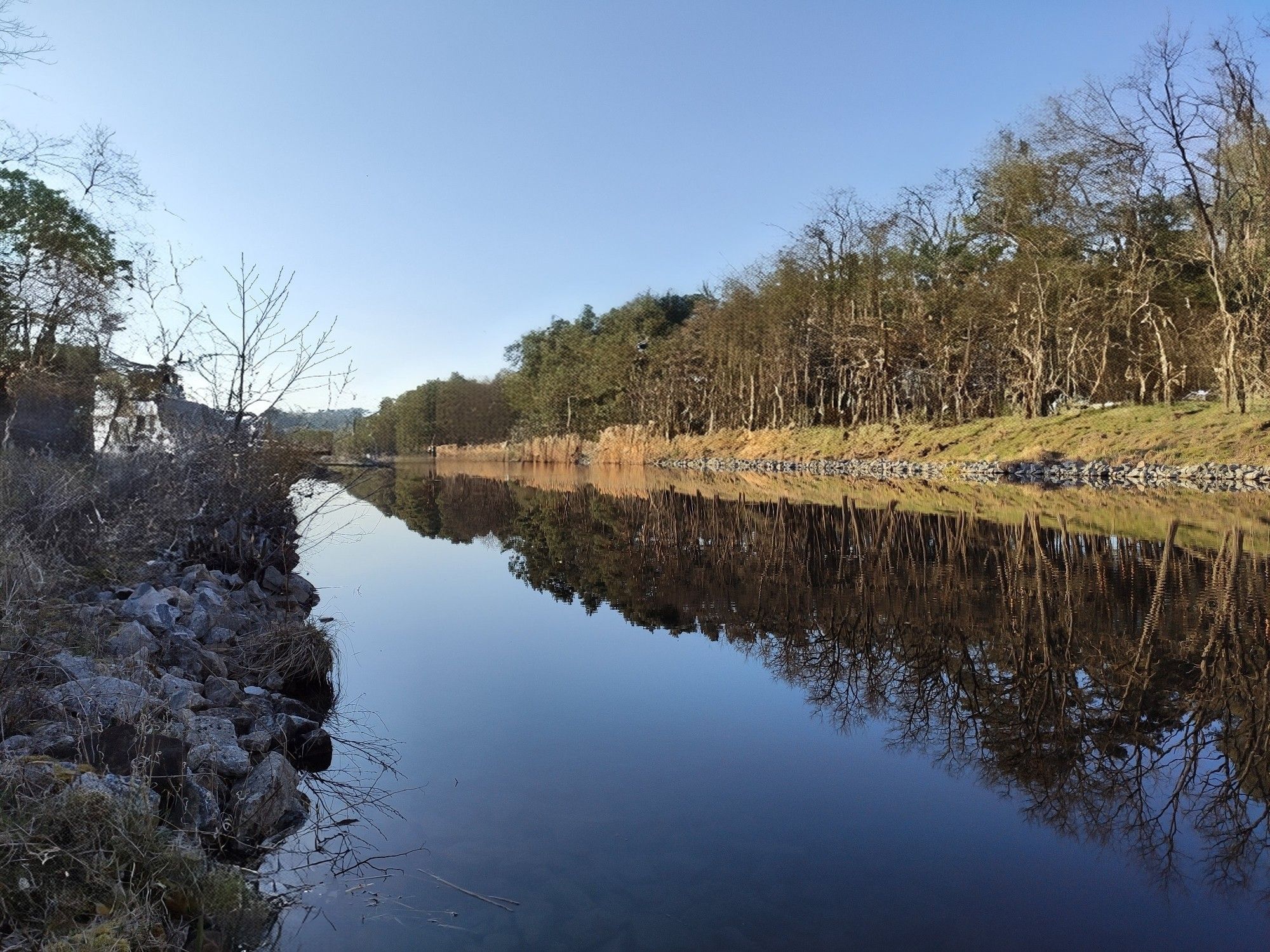 Kanal, vom Rand fotografiert. Strahlend blauer Himmel, Bäume spiegeln sich auf dem Wasser