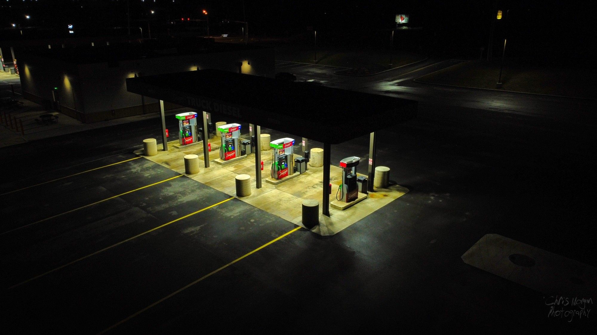 An aerial shot of four diesel pumps putting out warm light into the darkness of a small truckstop.