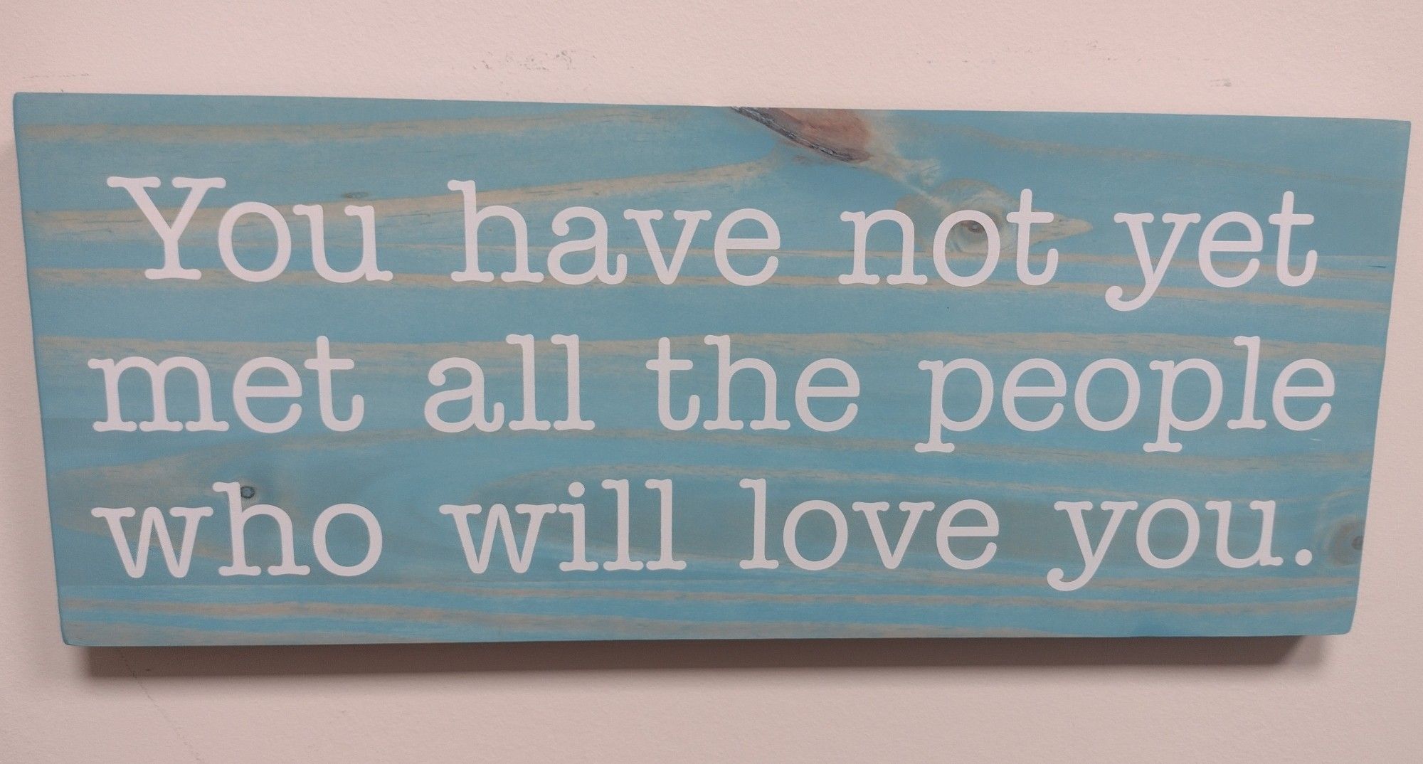 An engraved wood sign reading "you have not yet met all the people who will love you."