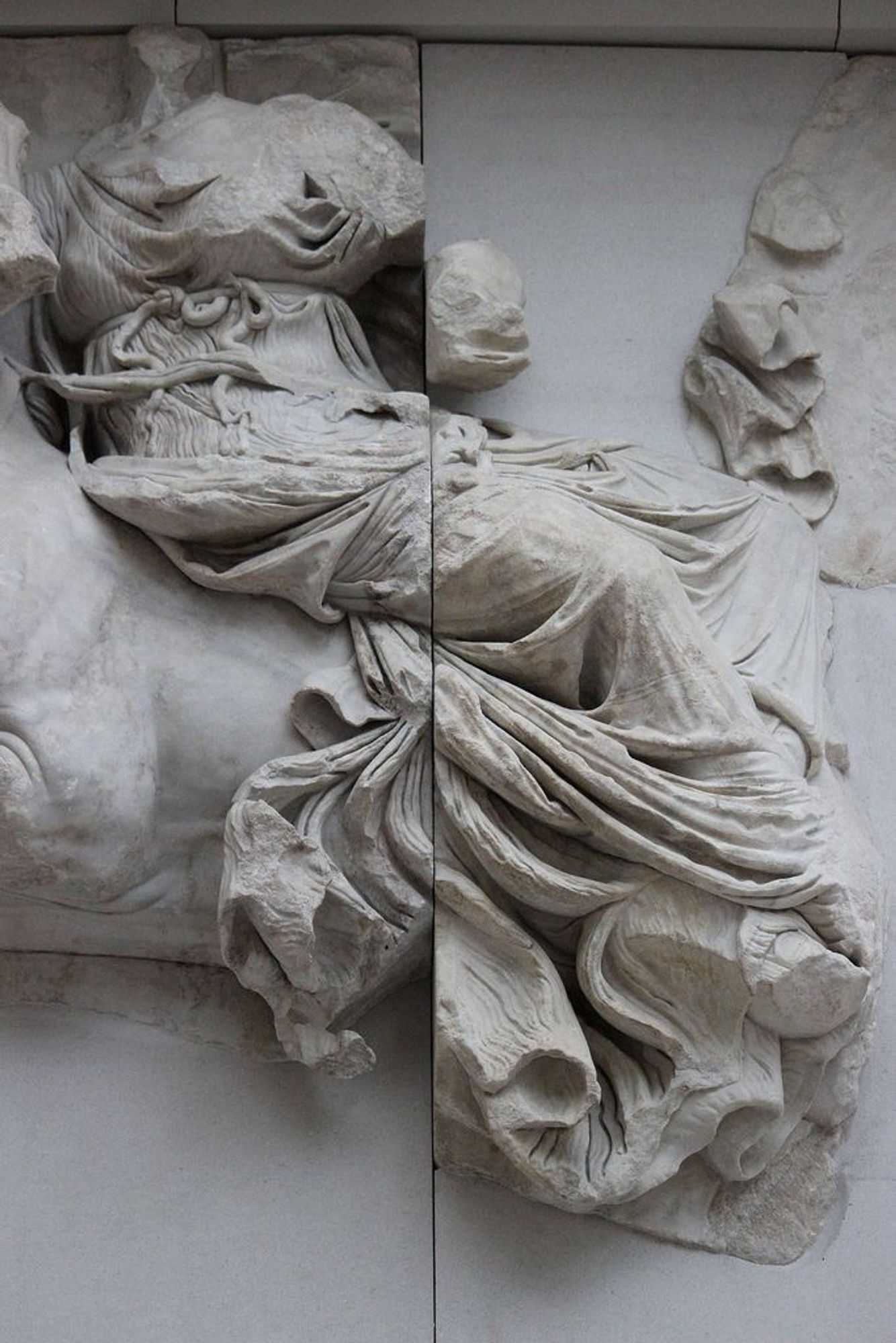 Fragment of a marble frieze showing a female figure thought to be the goddess Eos riding a horse. Her face and arms are missing. The figure wears a long gown with elaborate draping. From the Pergamon Altar, Pergamon Museum Berlin.