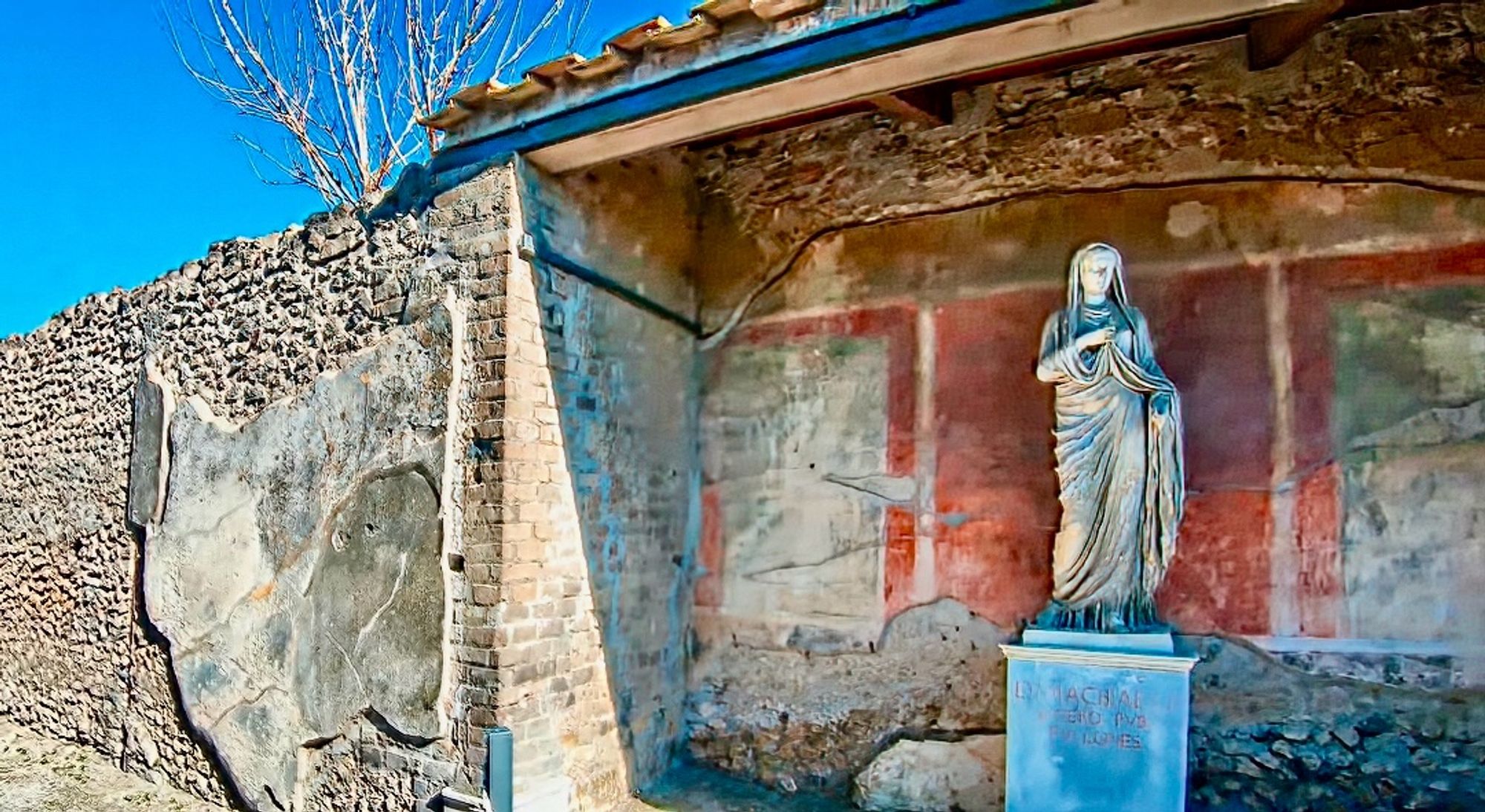 Statue of Eumachia on display in the remains of one of her buildings in Pompeii. The inscription reads ‘EVMACHIAE L F SACERD PVBL FVLLONES’: "to Eumachia, daughter of Lucius, public priestess of Pompeian Venus, from the fullers”. Image credit: Isaac Harjo of ProWalk Tours; Screen capture and additional editing by Mary Harrsch via Wikimedia Commons.